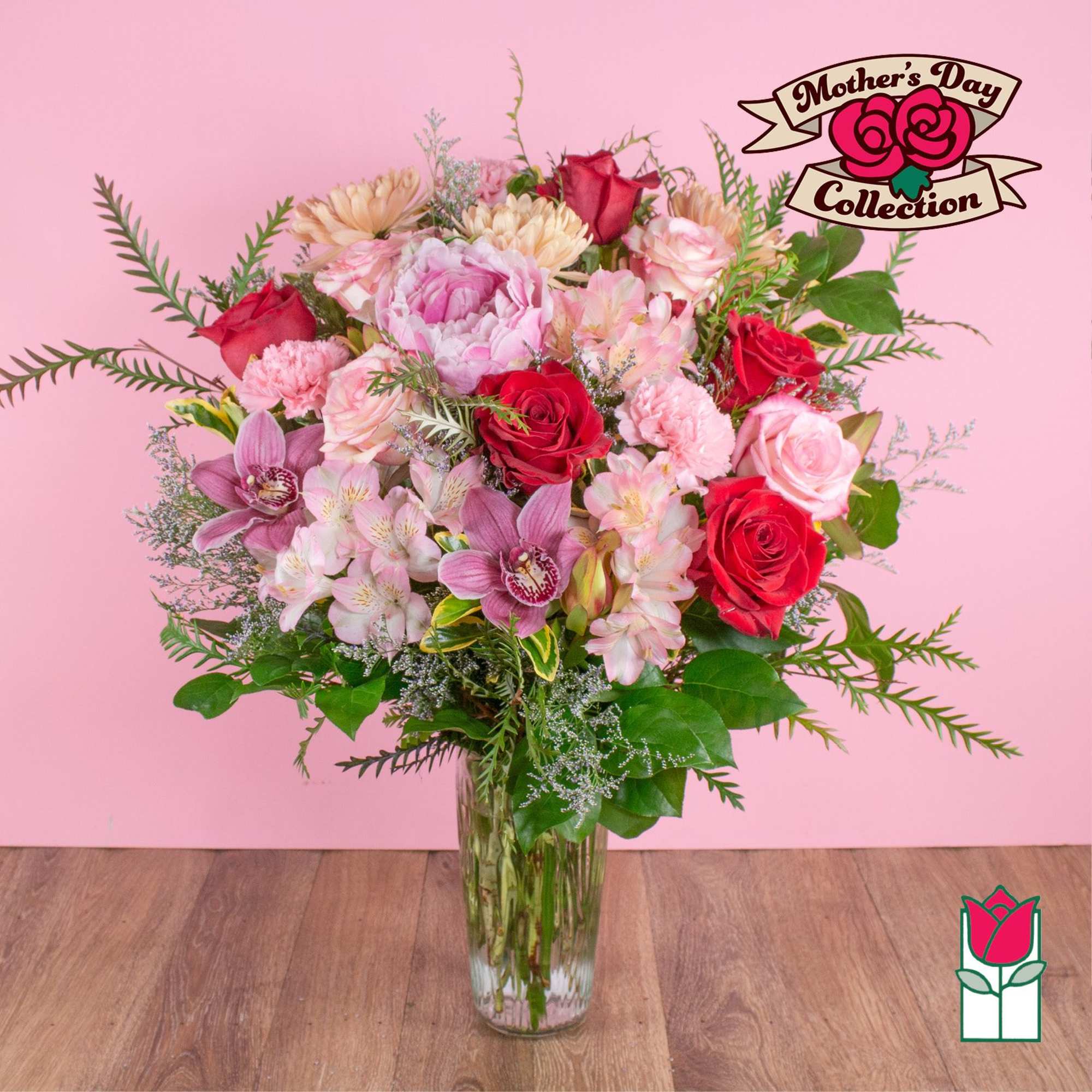 Tall vase arrangement of pink and red roses, orchids, carnations, and other flowers on a pink background
