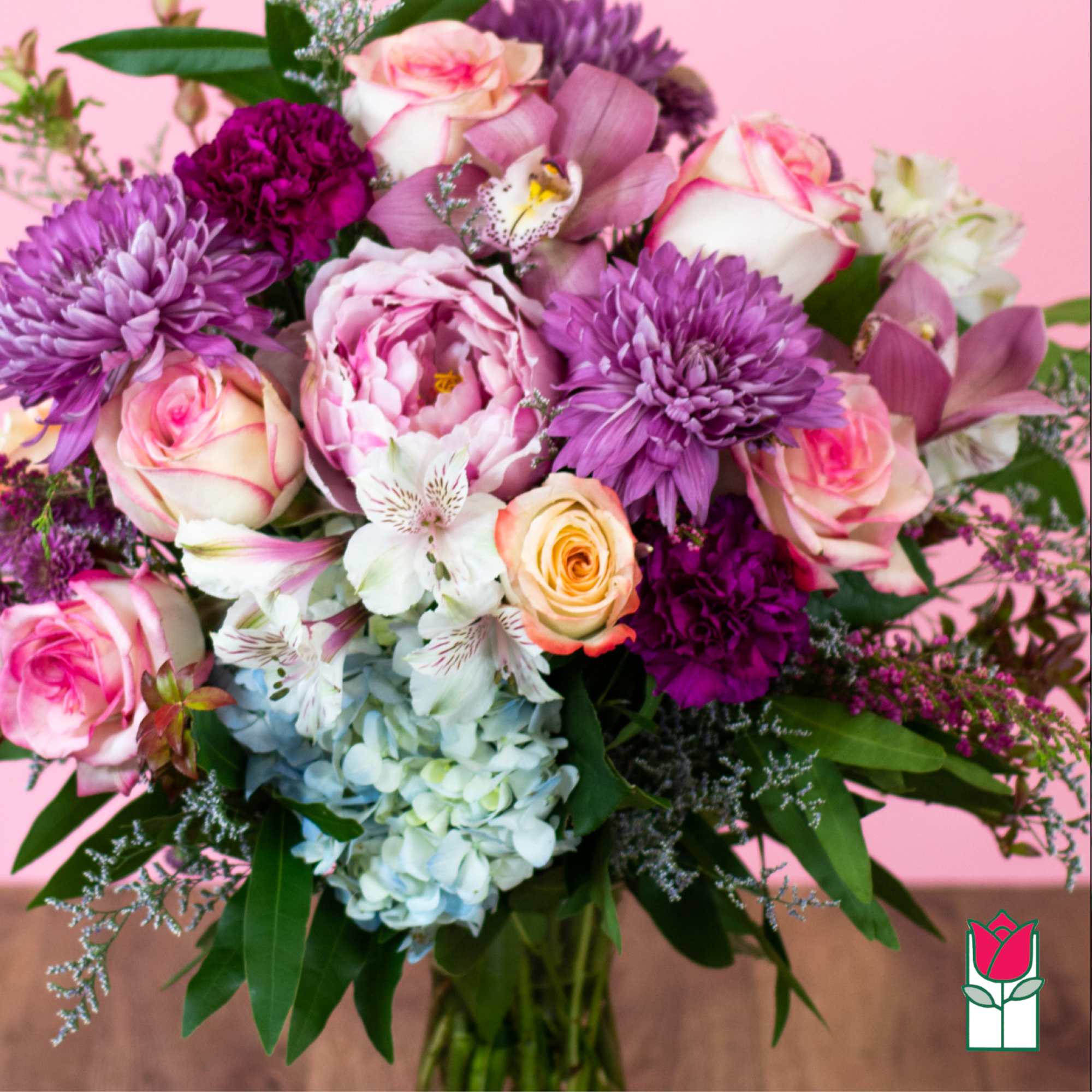 Mixed bouquet of pink roses, purple mums, blue hydrangea and white blooms in a glass vase