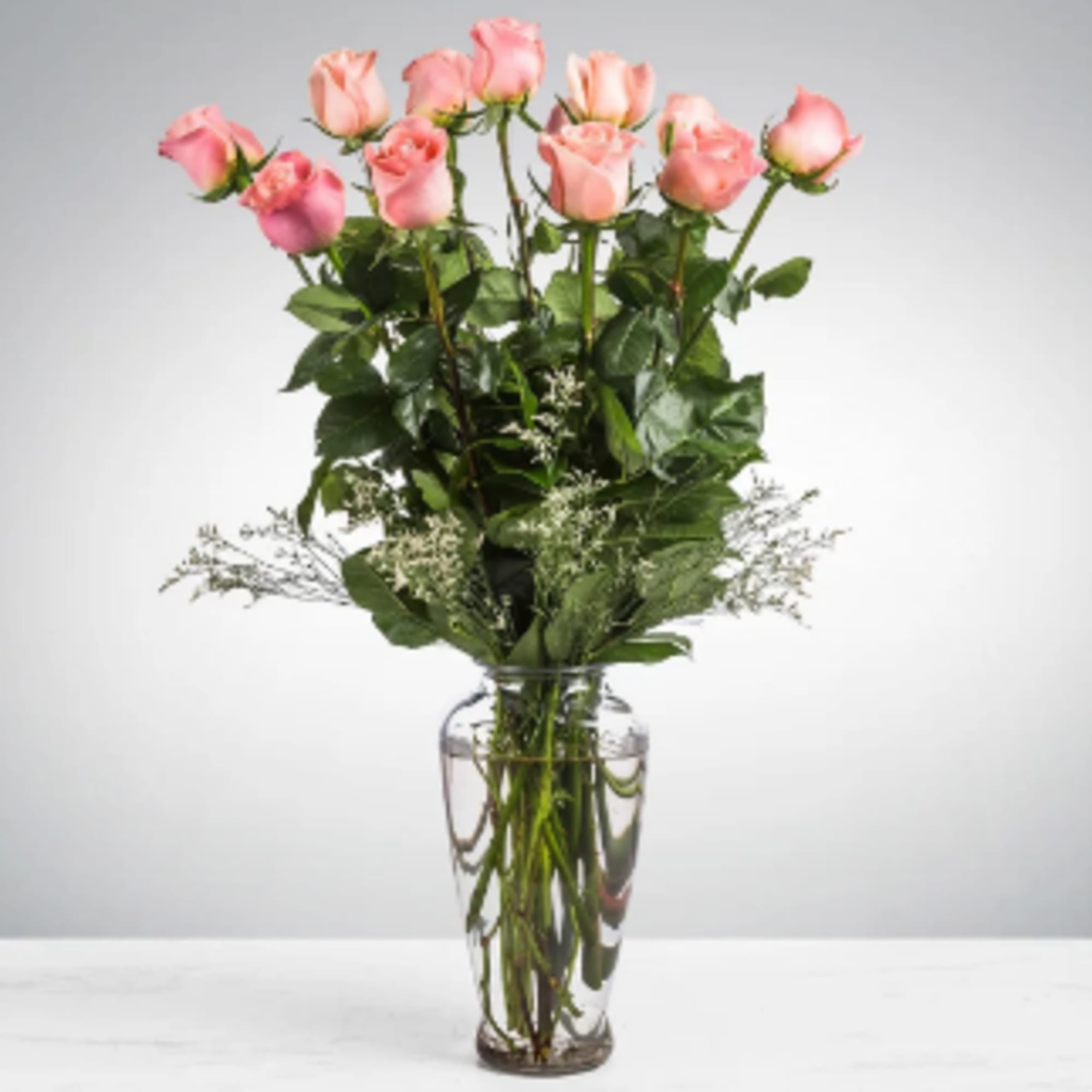 Tall arrangement of pink roses with white filler flowers in a clear glass vase