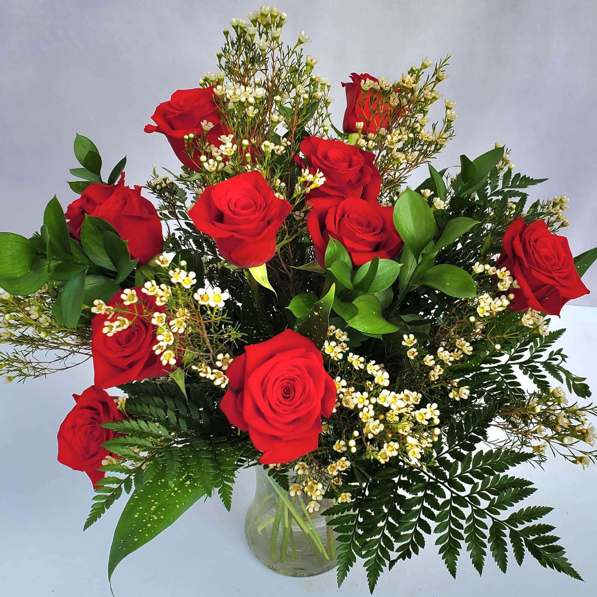 Arrangement of red roses with small white filler flowers in a clear glass vase