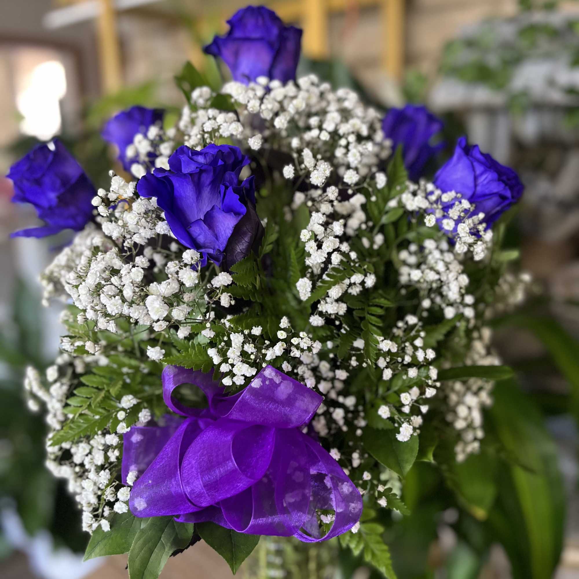 Arrangement of vivid purple roses with white filler flowers in a glass vase with a purple bow.
