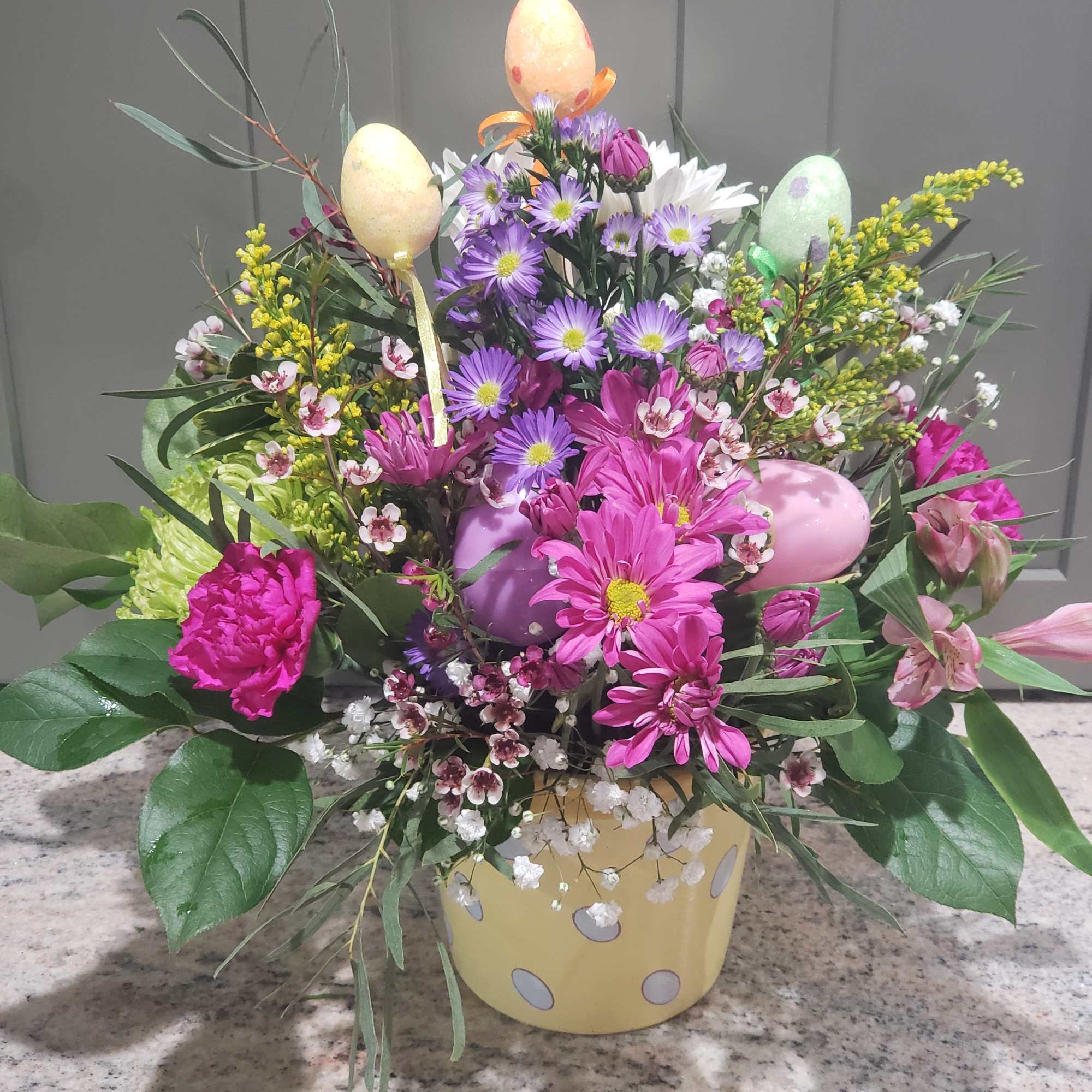 Colorful mixed spring flowers with pastel decorative eggs in a yellow polka dot pot