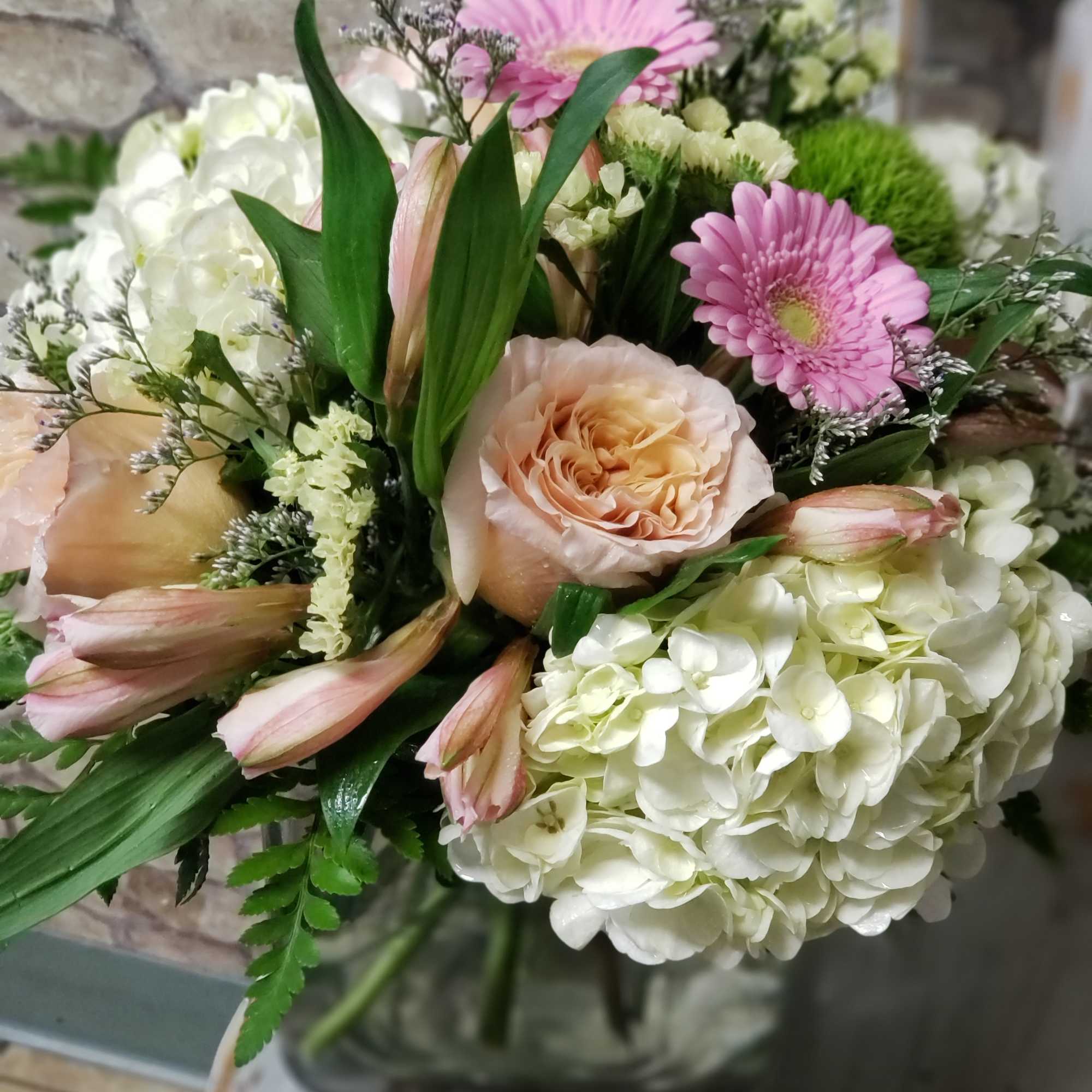 Pastel bouquet of white hydrangeas, peach roses, and pink gerbera daisies in a clear glass vase.