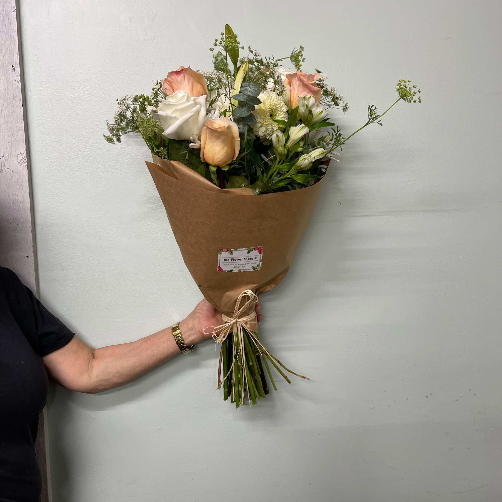 Hand-tied bouquet of peach and white roses and mixed white flowers wrapped in kraft paper