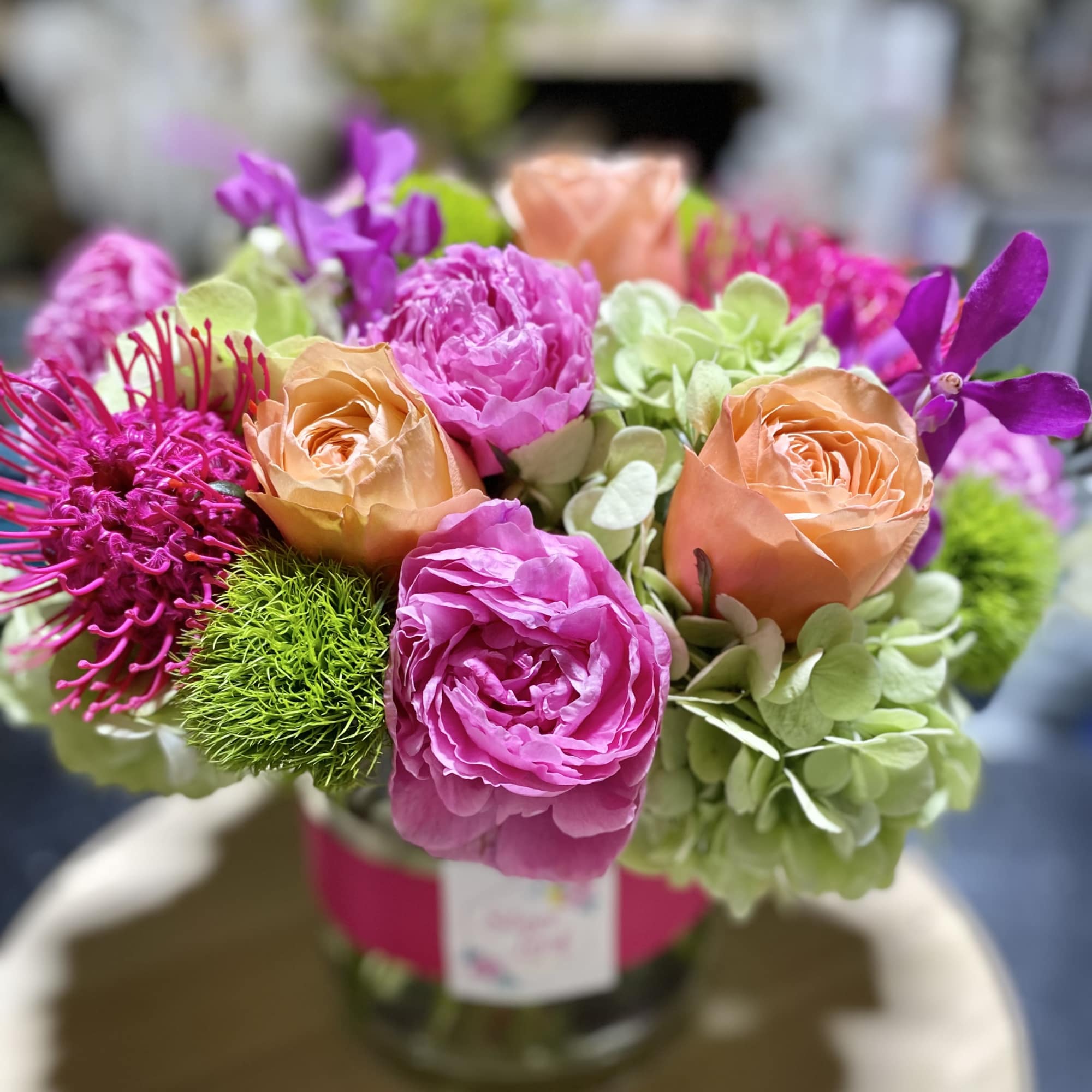Low glass vase of peach roses, bright pink blooms, green hydrangeas, and purple accents