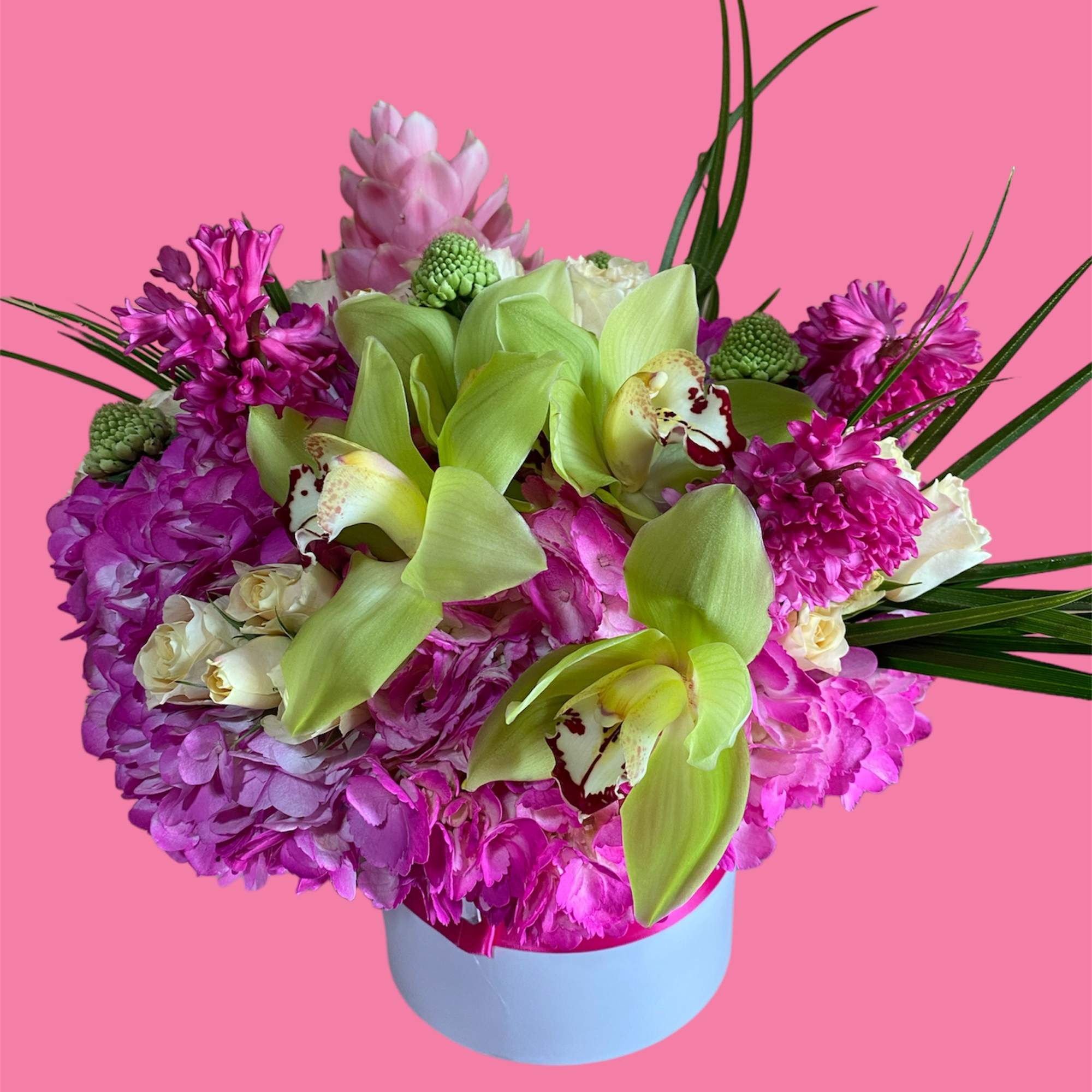 Compact hatbox arrangement of green cymbidium orchids, pink hydrangeas, and cream roses in a white container.