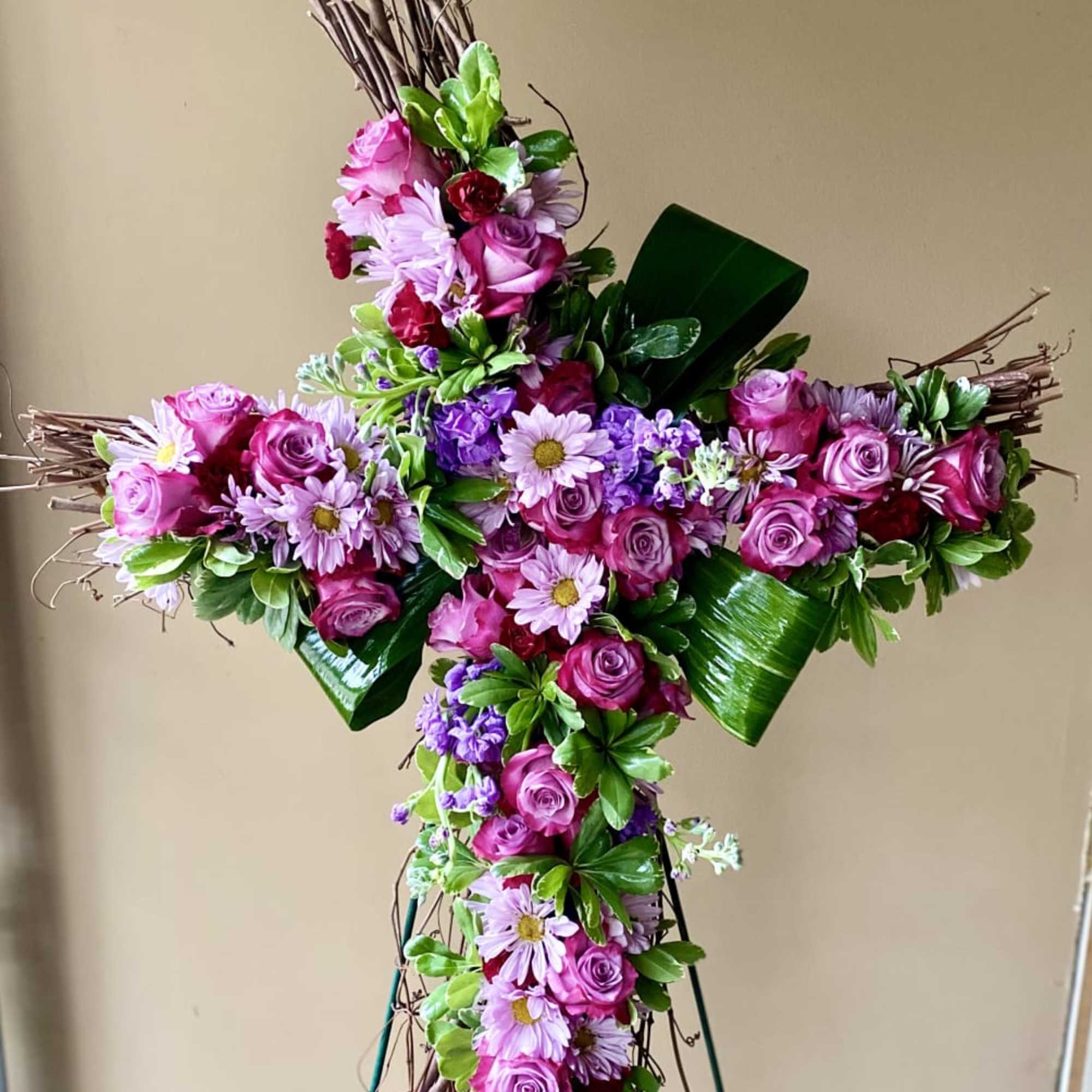 Standing cross-shaped spray of pink roses and purple daisies on a twig base with folded green leaves.