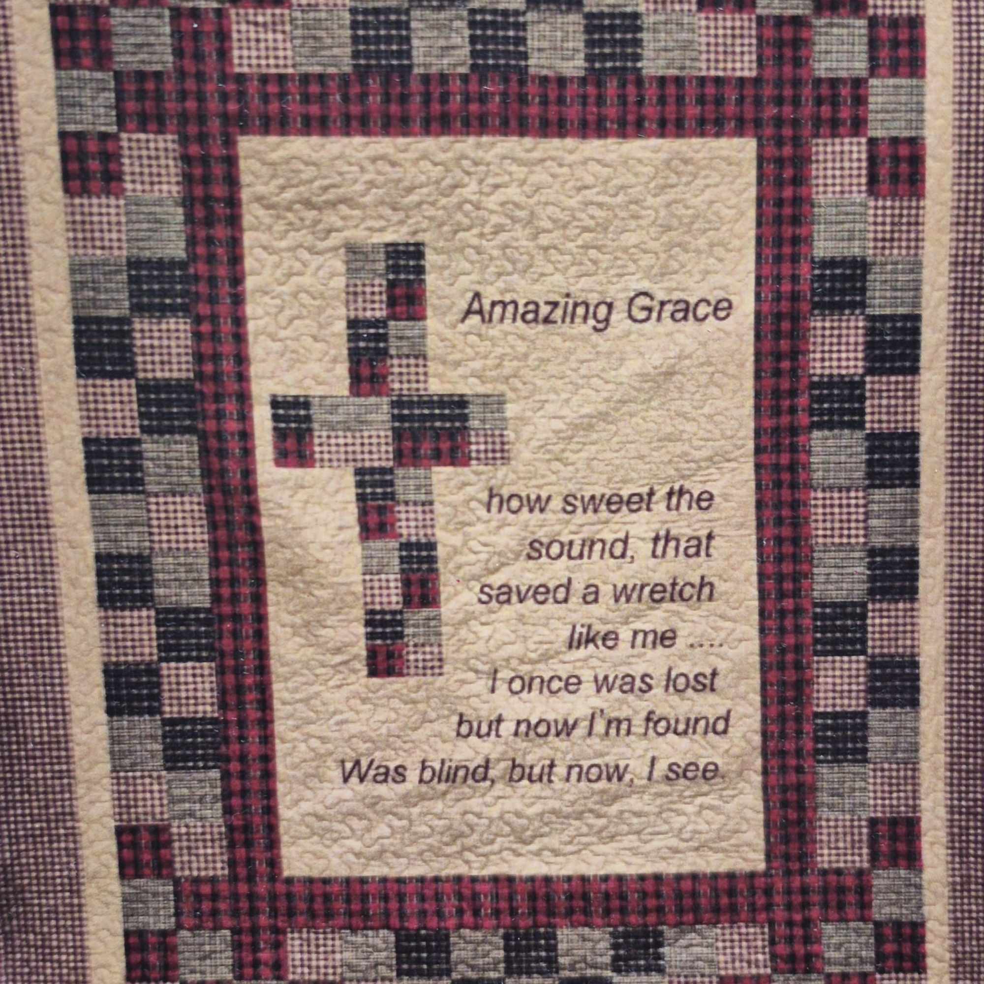 A handcrafted quilted wall hanging centered with a patchwork cross in red