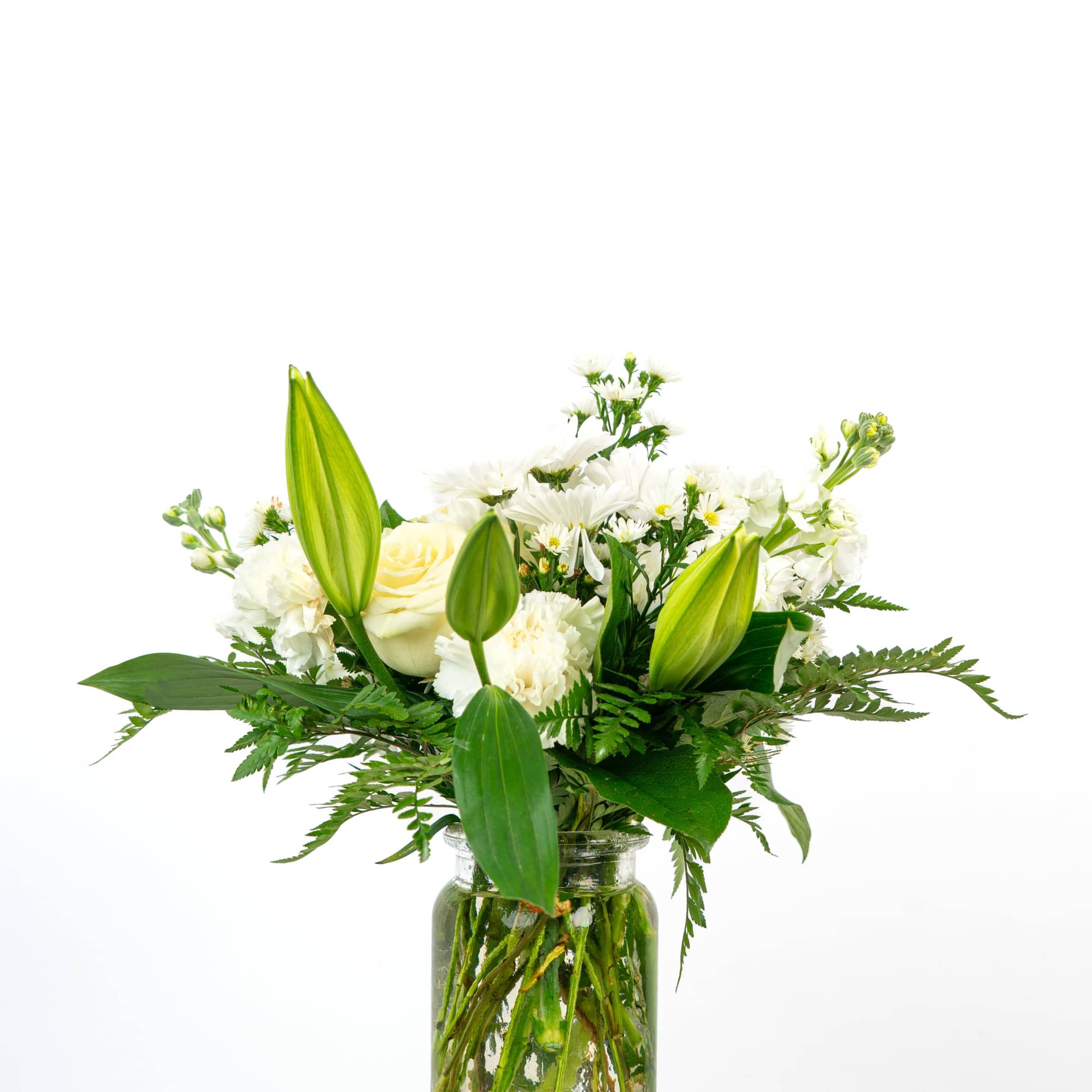 White lilies, roses, and other white flowers arranged in a clear glass jar vase