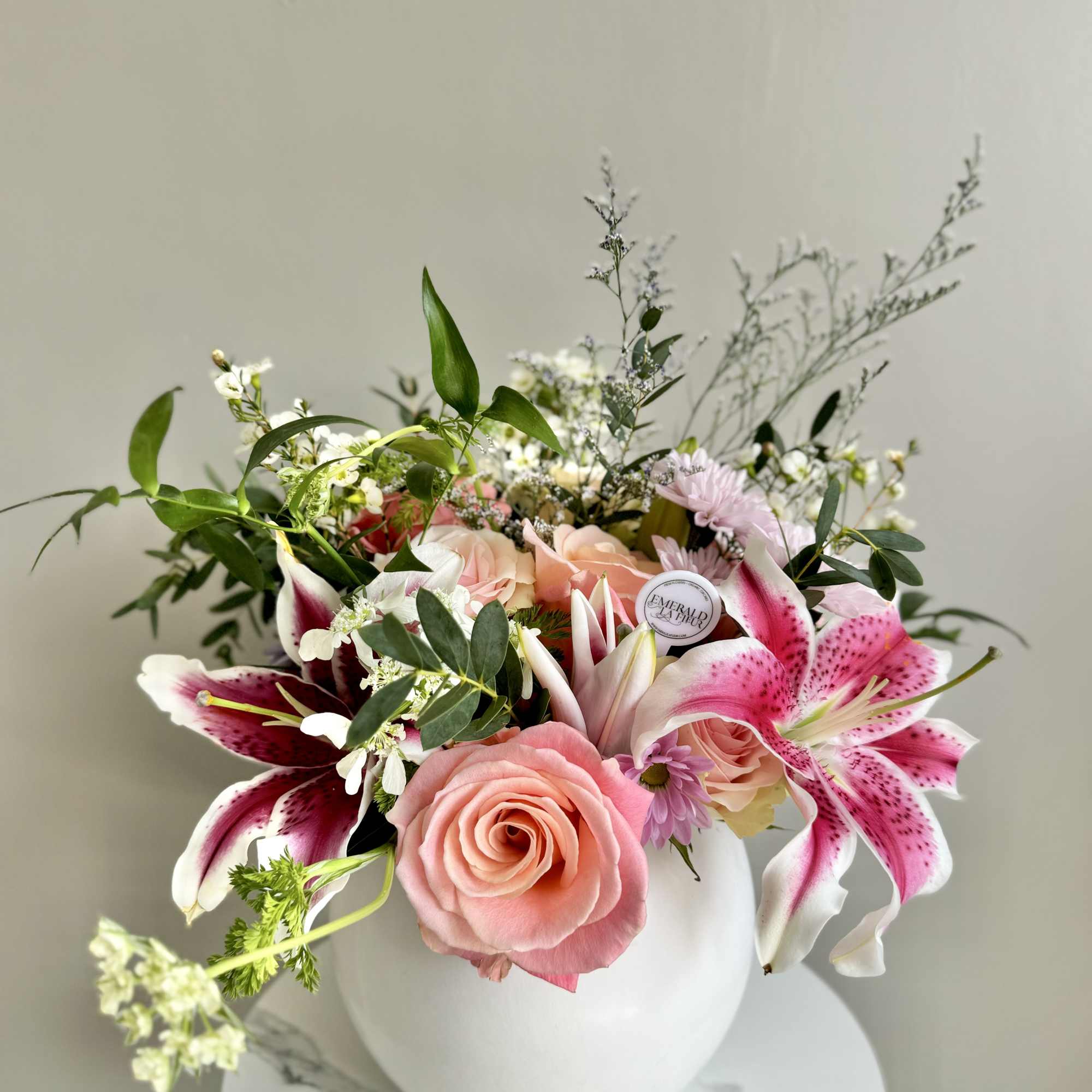 Pink roses and stargazer lilies with white filler flowers in a round white vase