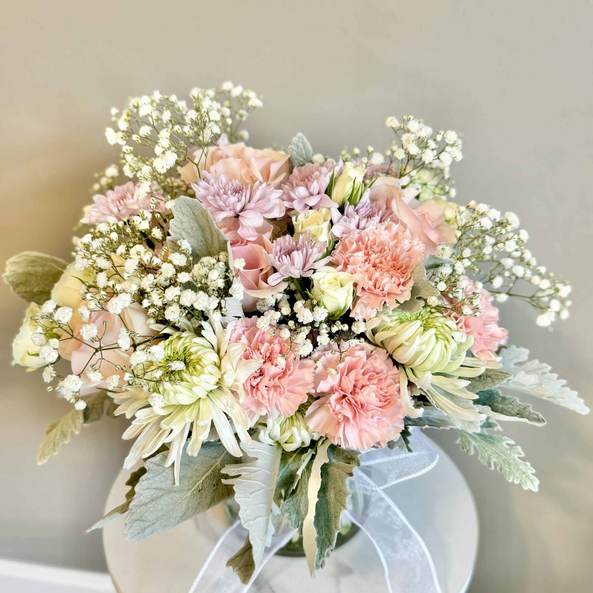 Pastel pink and white bouquet with carnations, roses, and mums in a glass vase with ribbon