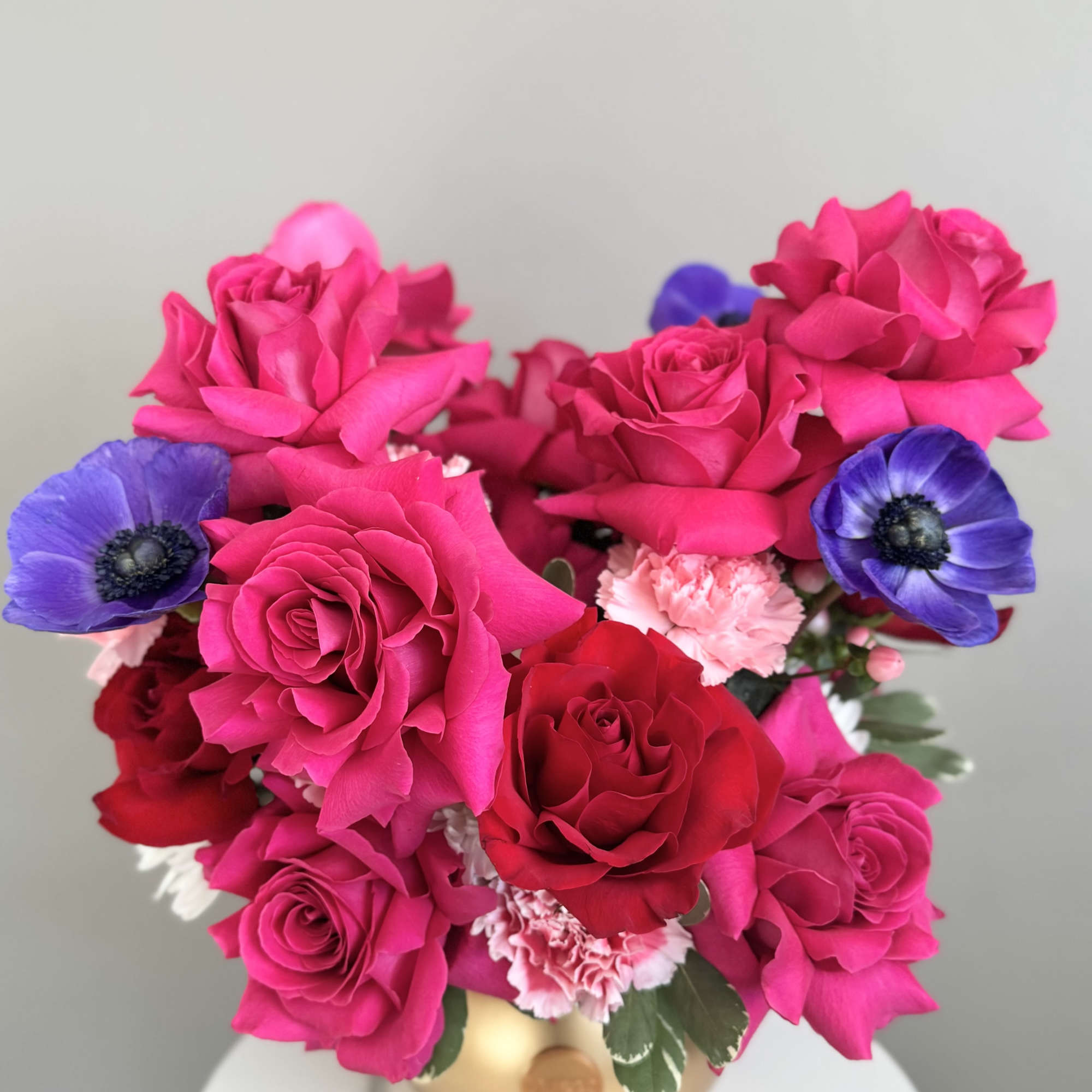 Low arrangement of hot pink and red roses with pink carnations and purple anemones in a gold bowl vase