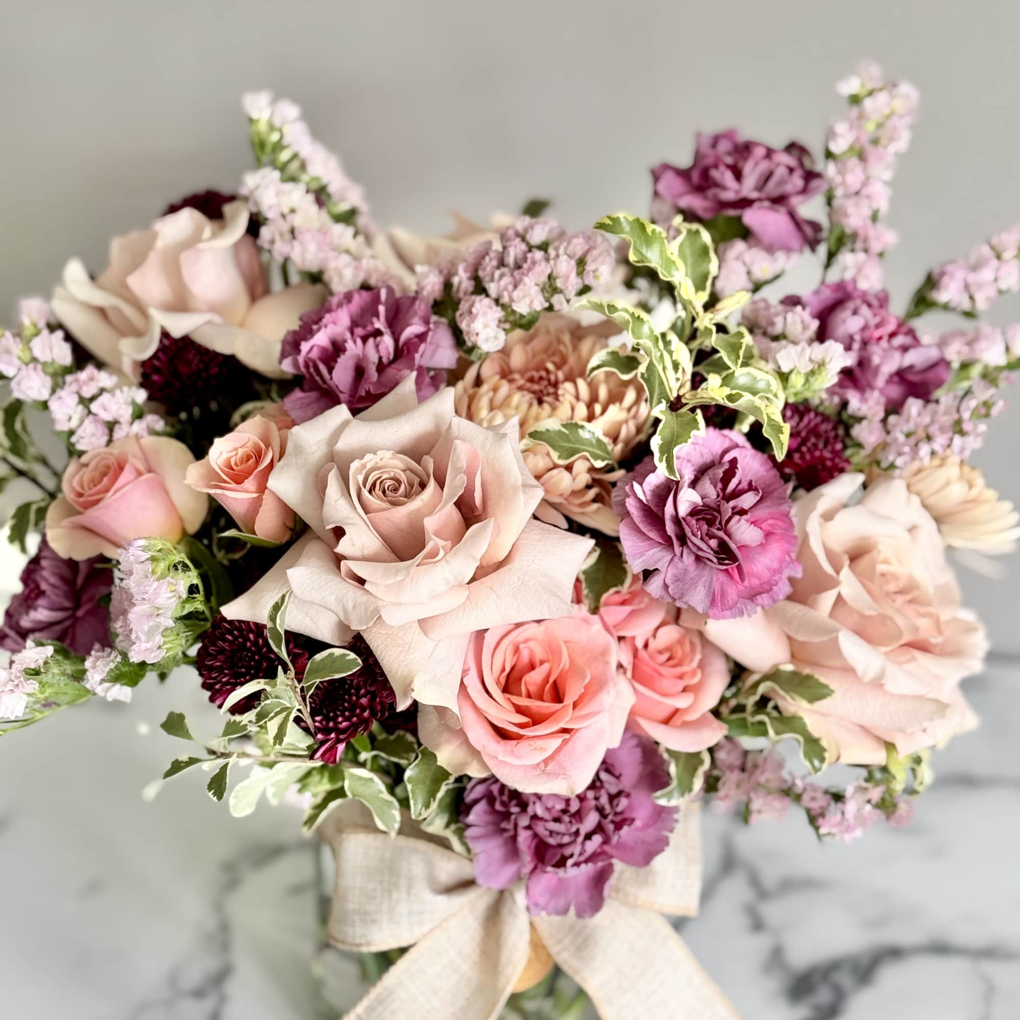 Pink and purple bouquet with roses and carnations in a glass vase with a linen bow.