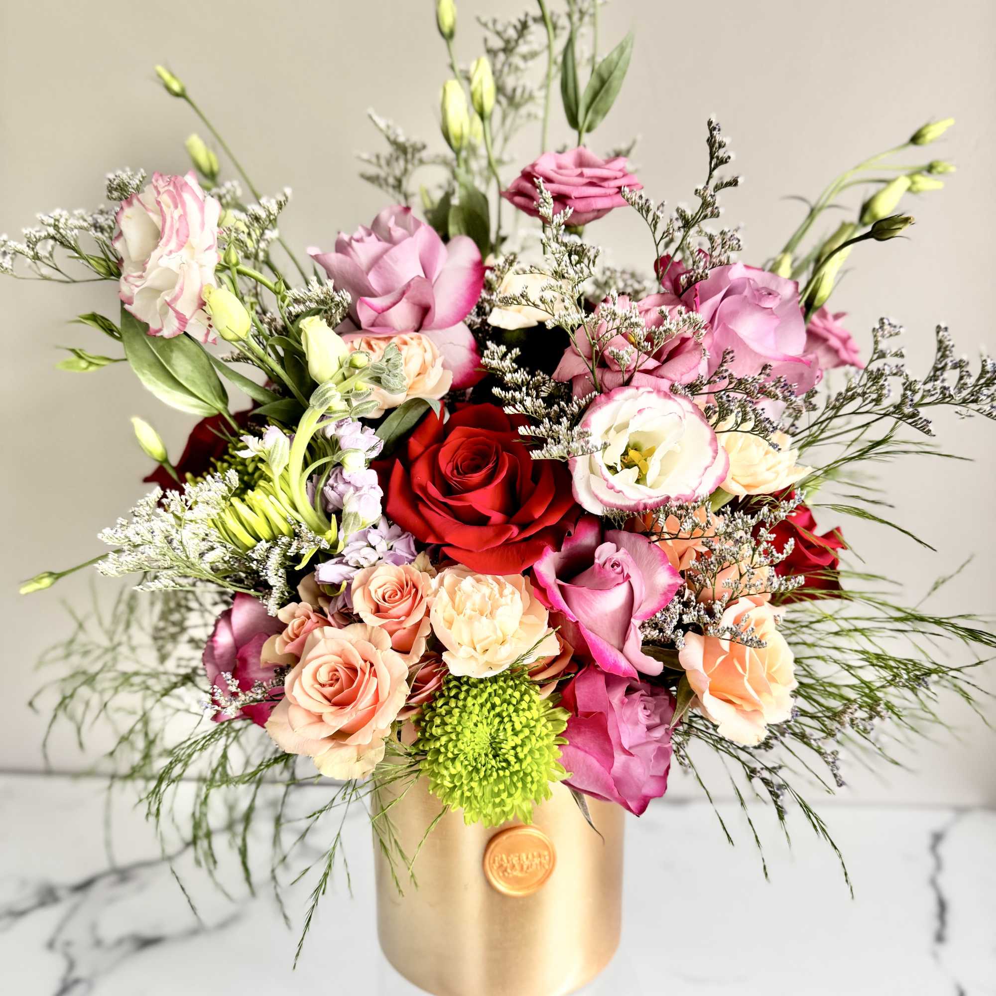 Mixed arrangement of pink, red, and peach roses with lisianthus in a gold cylinder vase