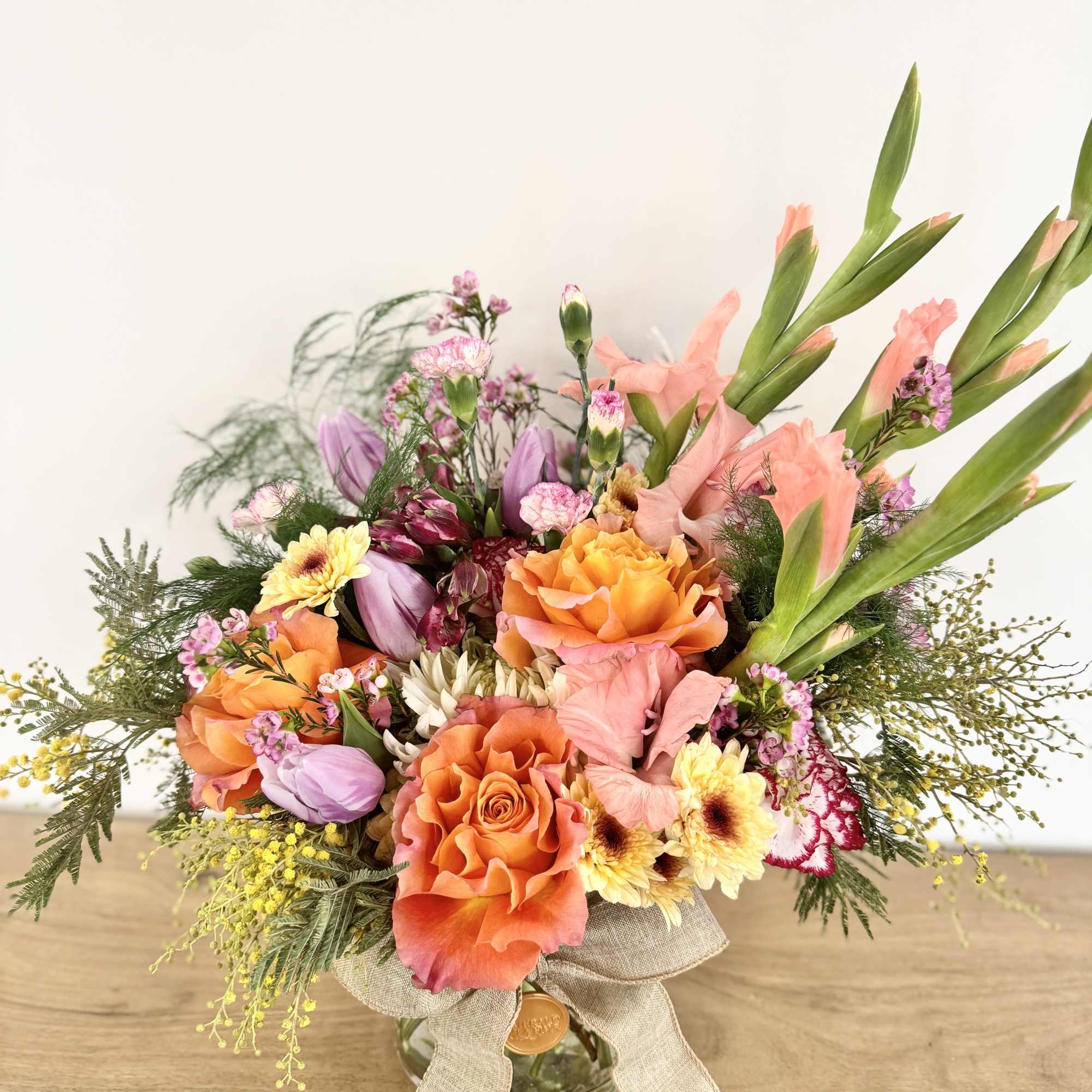Bright mixed bouquet with orange roses, tulips, and peach blooms in a glass vase with a bow.