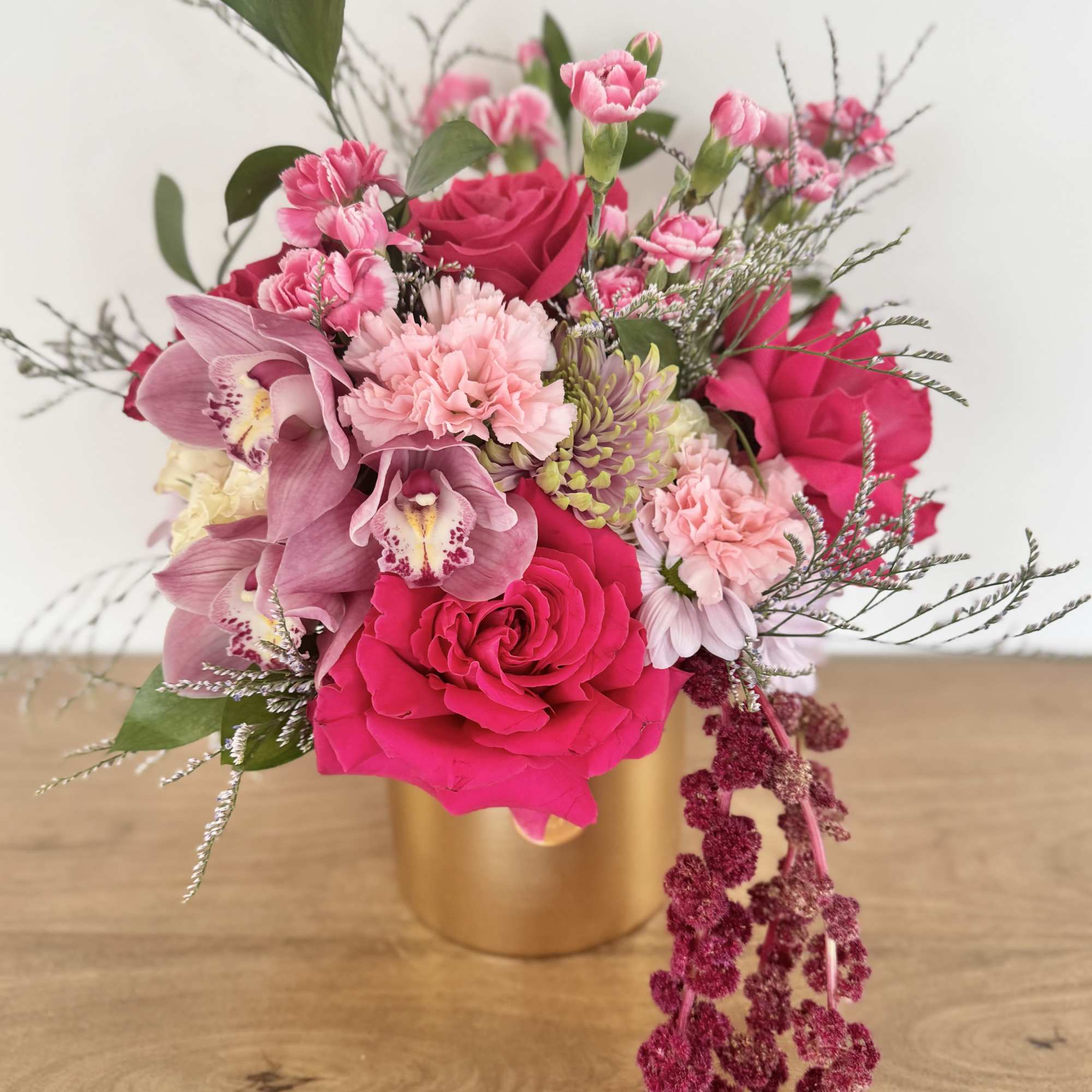 Pink rose and orchid arrangement in a gold vase on a wooden table