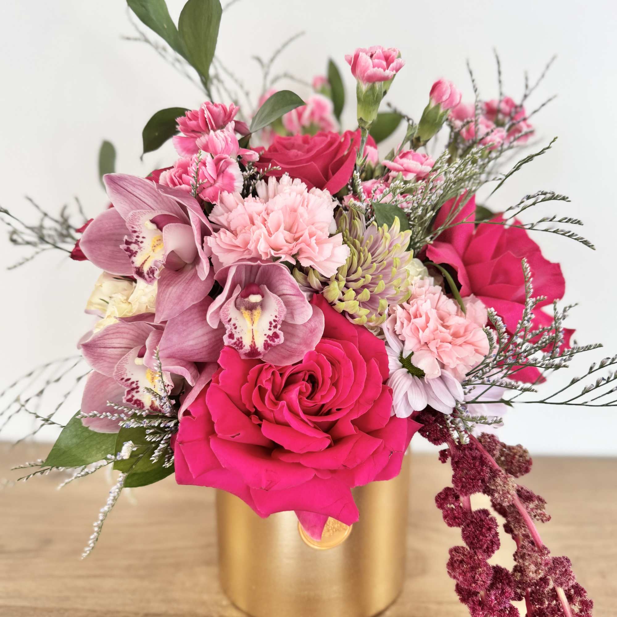 Pink roses, carnations, orchids, and mums arranged in a gold cylinder vase