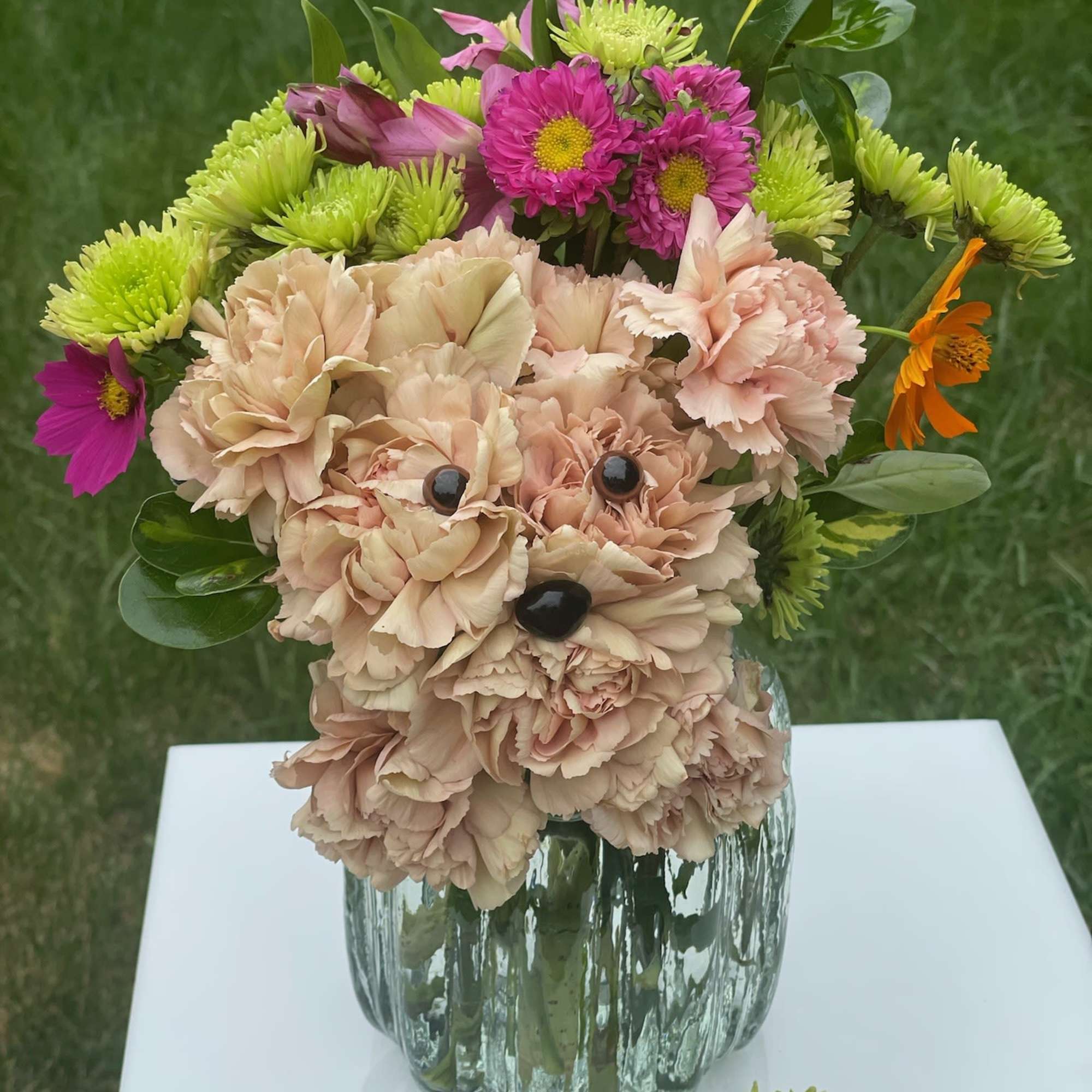Peach carnation dog-shaped arrangement with bright green and magenta mums in a ribbed glass vase