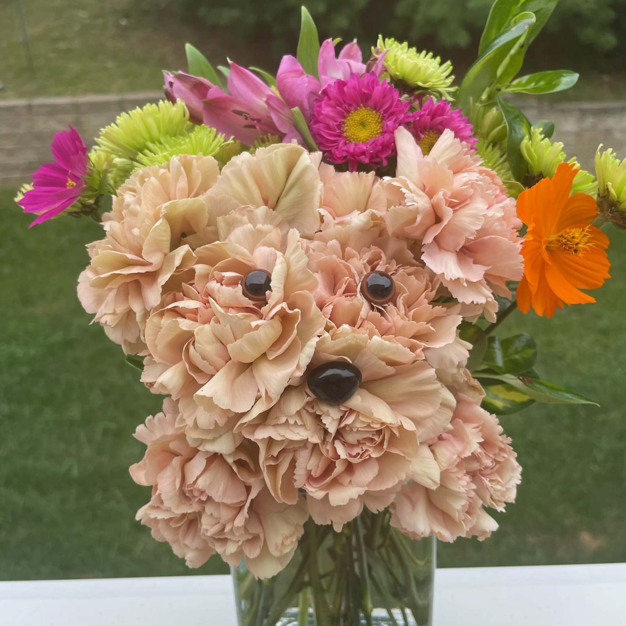 Square vase of peach carnations shaped like a puppy with bright pink, orange, and green accent flowers.