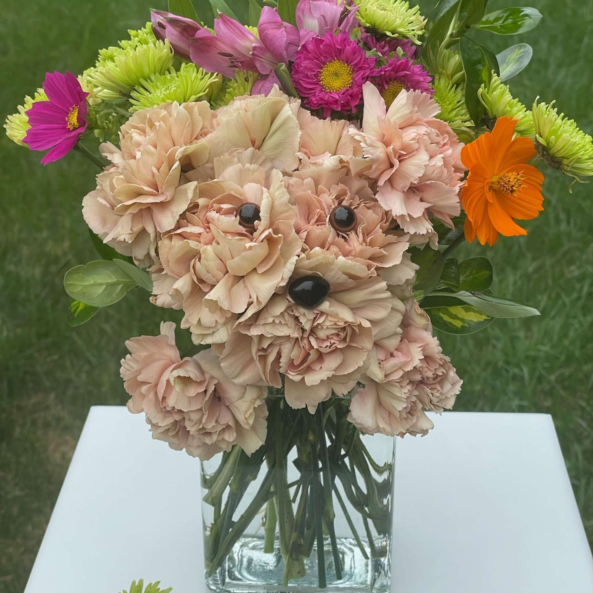 Dog-shaped arrangement of blush carnations with bright mixed flowers in a clear glass vase