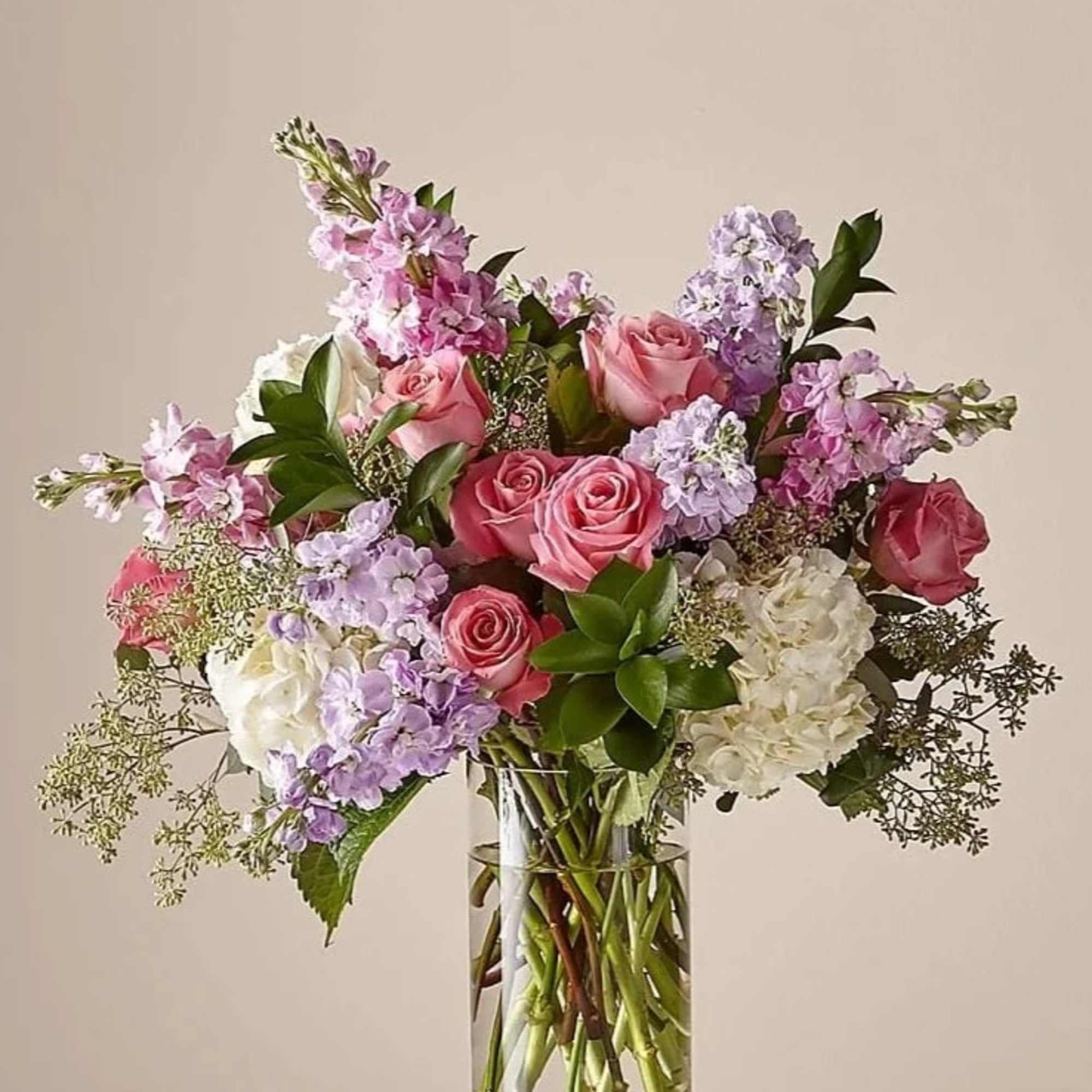 Tall glass vase of pink roses, white hydrangeas, and light purple flowers.