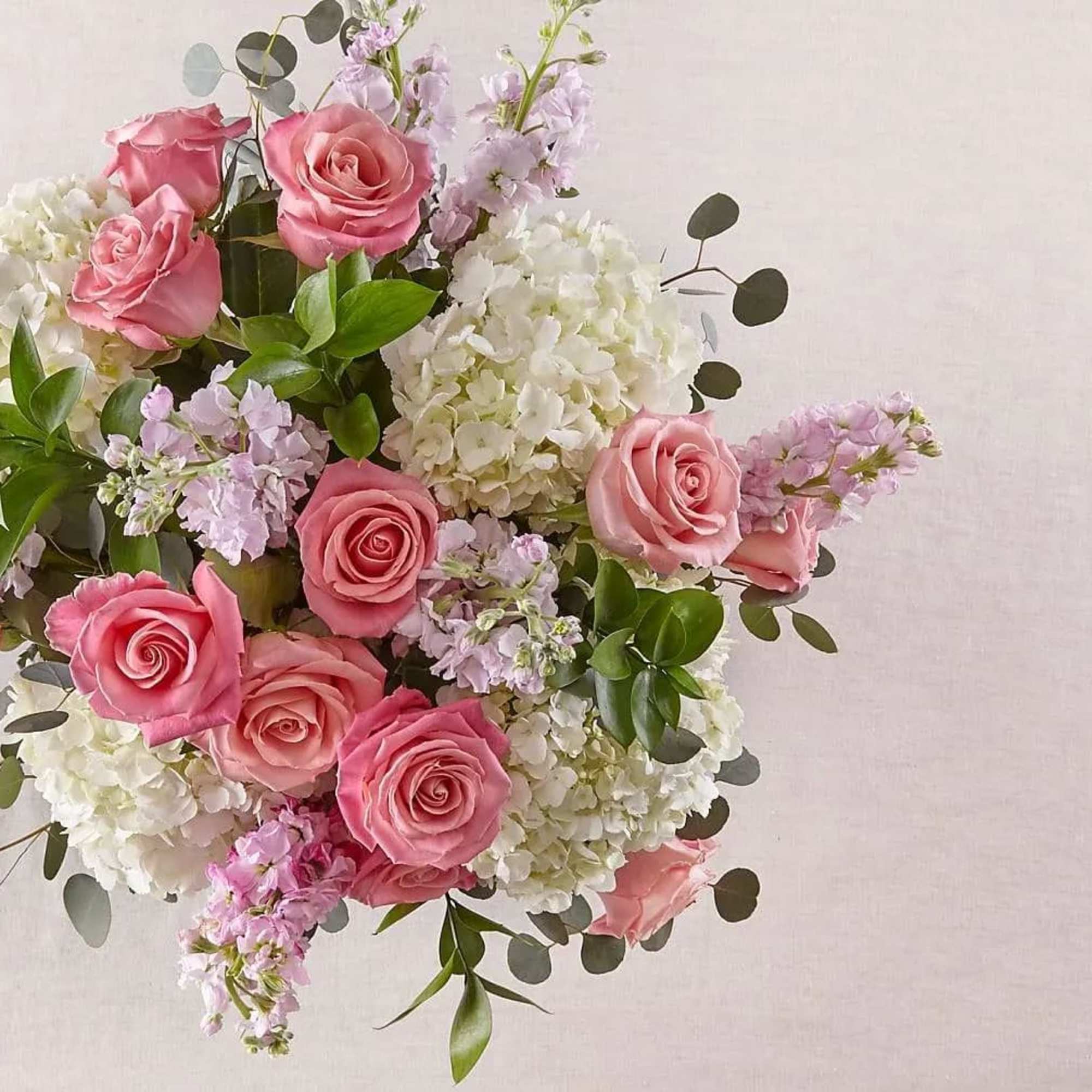 Arrangement of pink roses, white hydrangeas, and soft lavender flowers in a rounded pastel bouquet