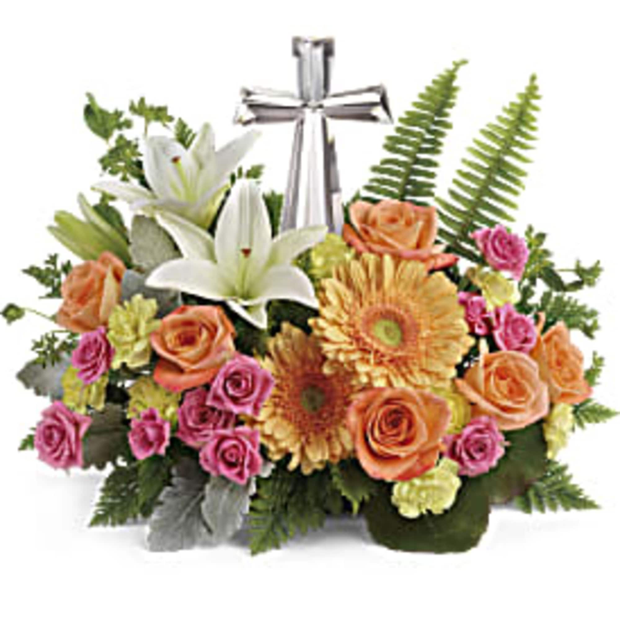 Low mixed arrangement of lilies, roses, and daisies with pastel blooms around a silver cross figurine