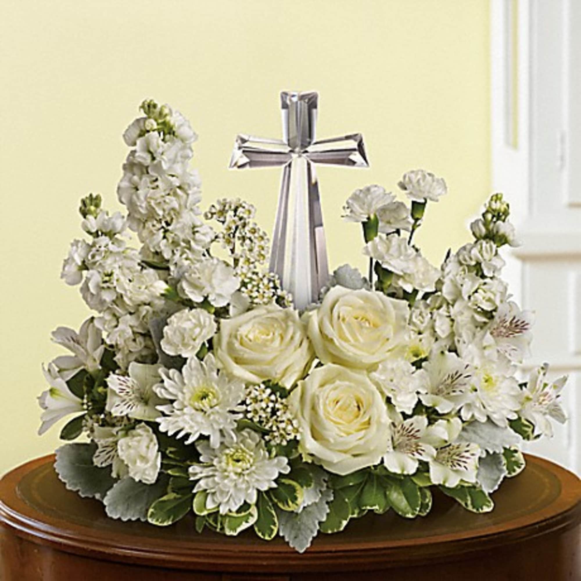 White floral arrangement with roses and a clear crystal cross on a low container