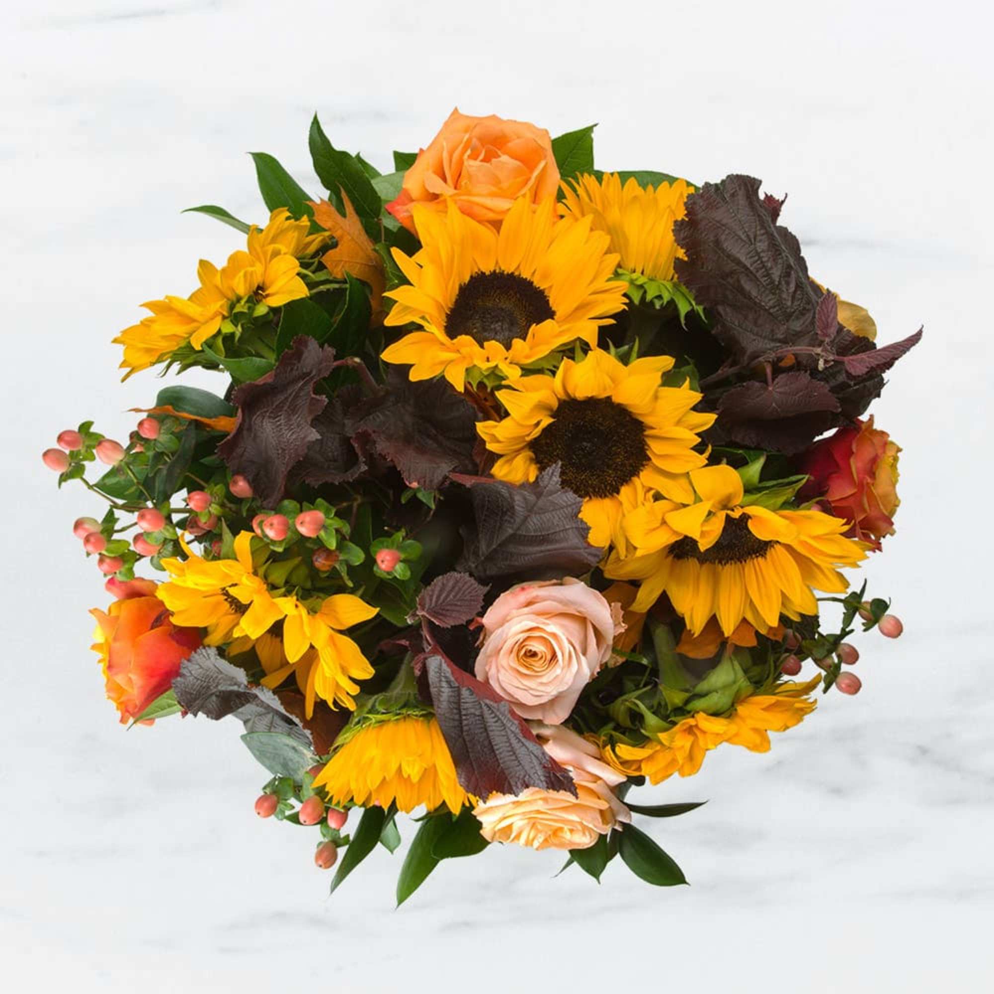 Bouquet of bright yellow sunflowers and peach roses with dark accent foliage