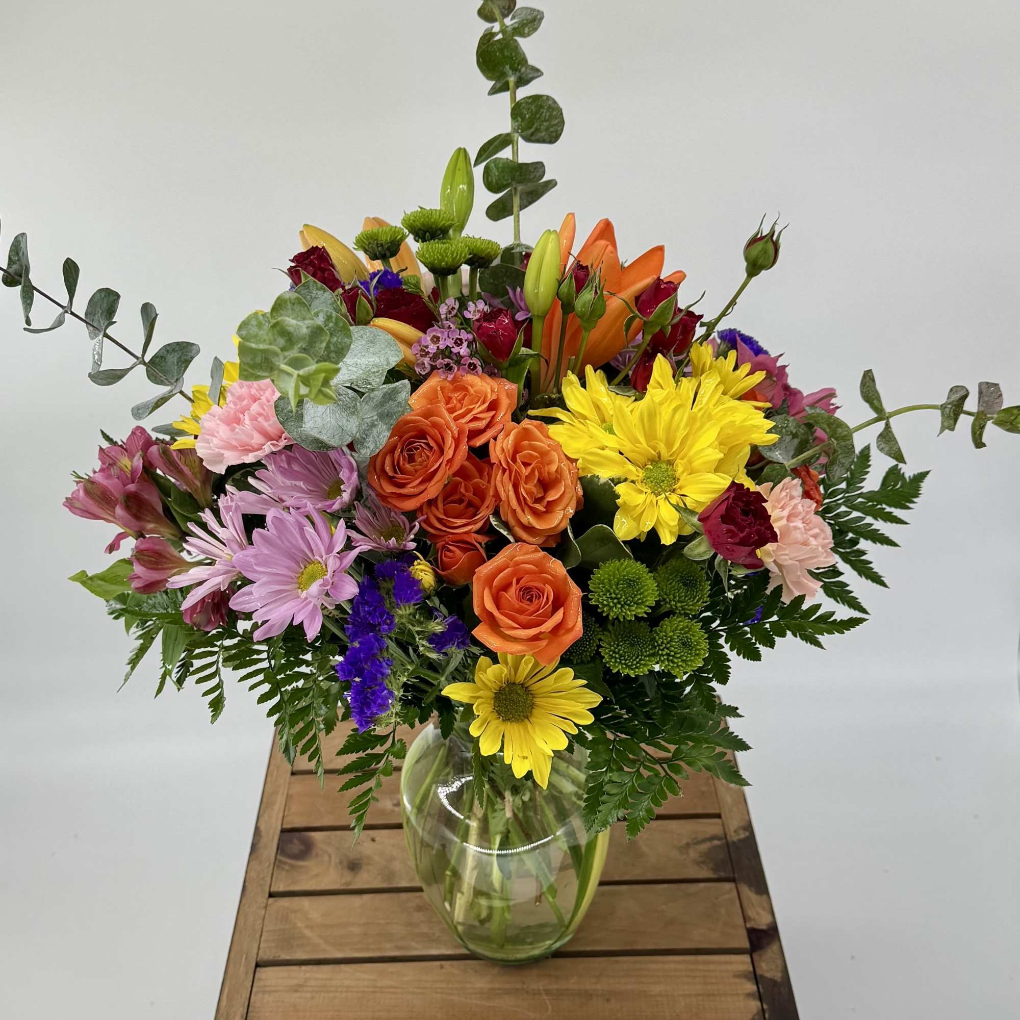 This vibrant modern floral arrangement features orange lilies, yellow and lavender daisies