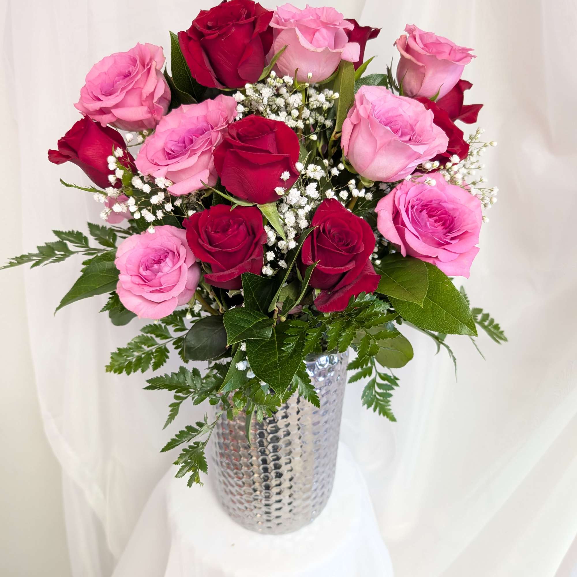 Arrangement of red and pink roses with white filler in a tall silver vase