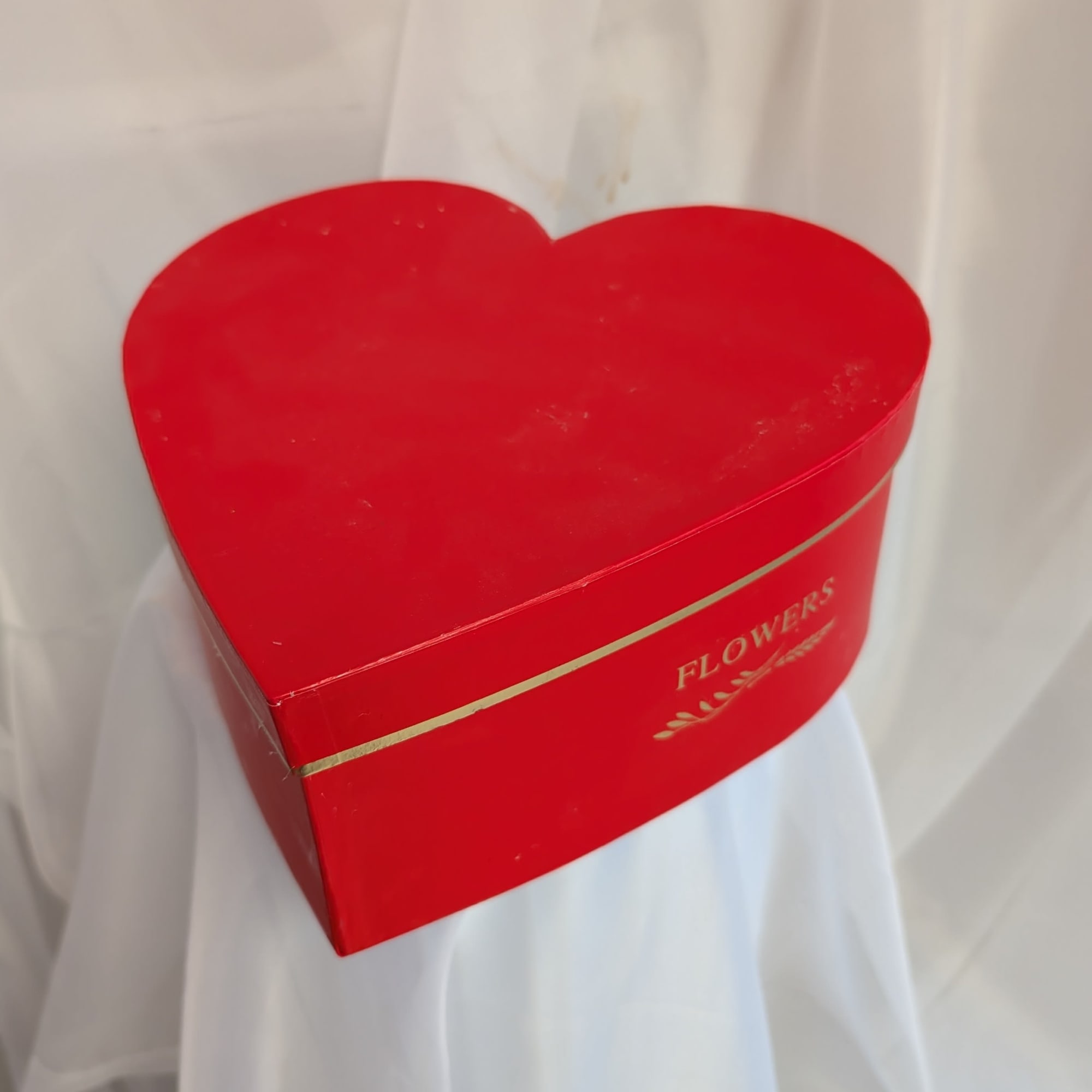 Red heart-shaped flower box with gold lettering on a white fabric backdrop