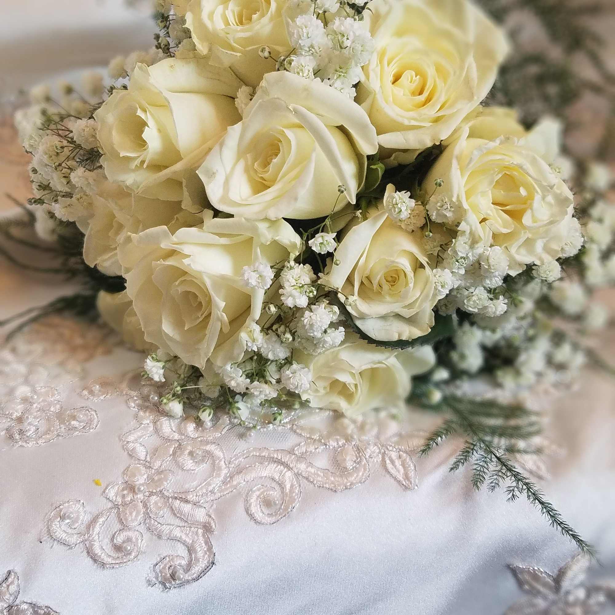 Bridal bouquet of ivory roses and baby's breath resting on embroidered white lace fabric