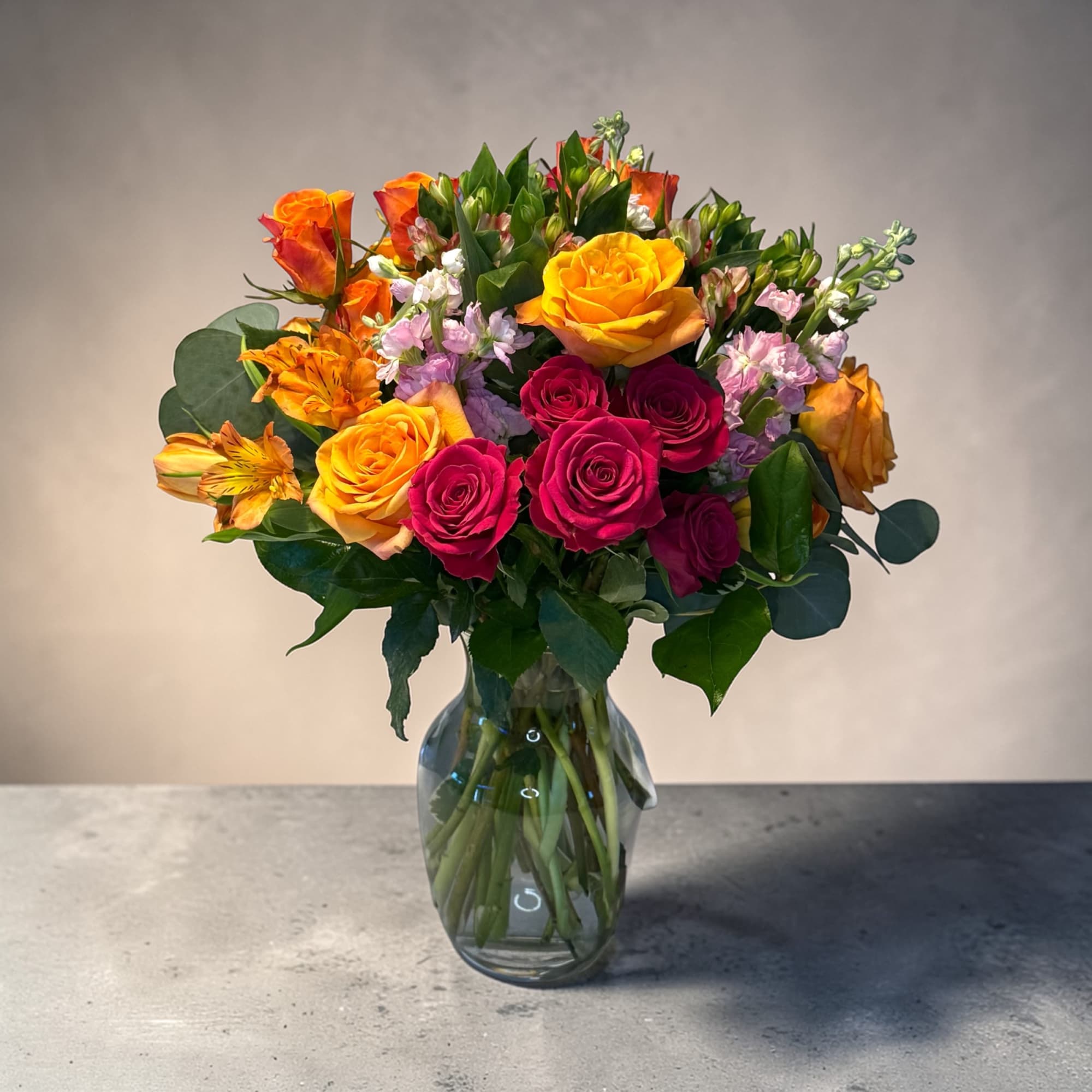 A vibrant cluster of yellow, orange, and deep pink roses crowns this