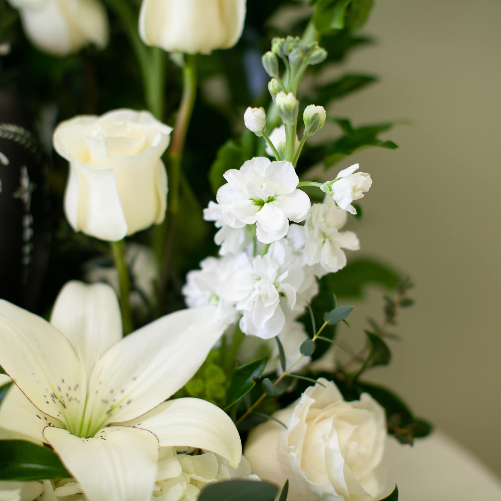 White lilies and roses arranged beside a dark decorative urn