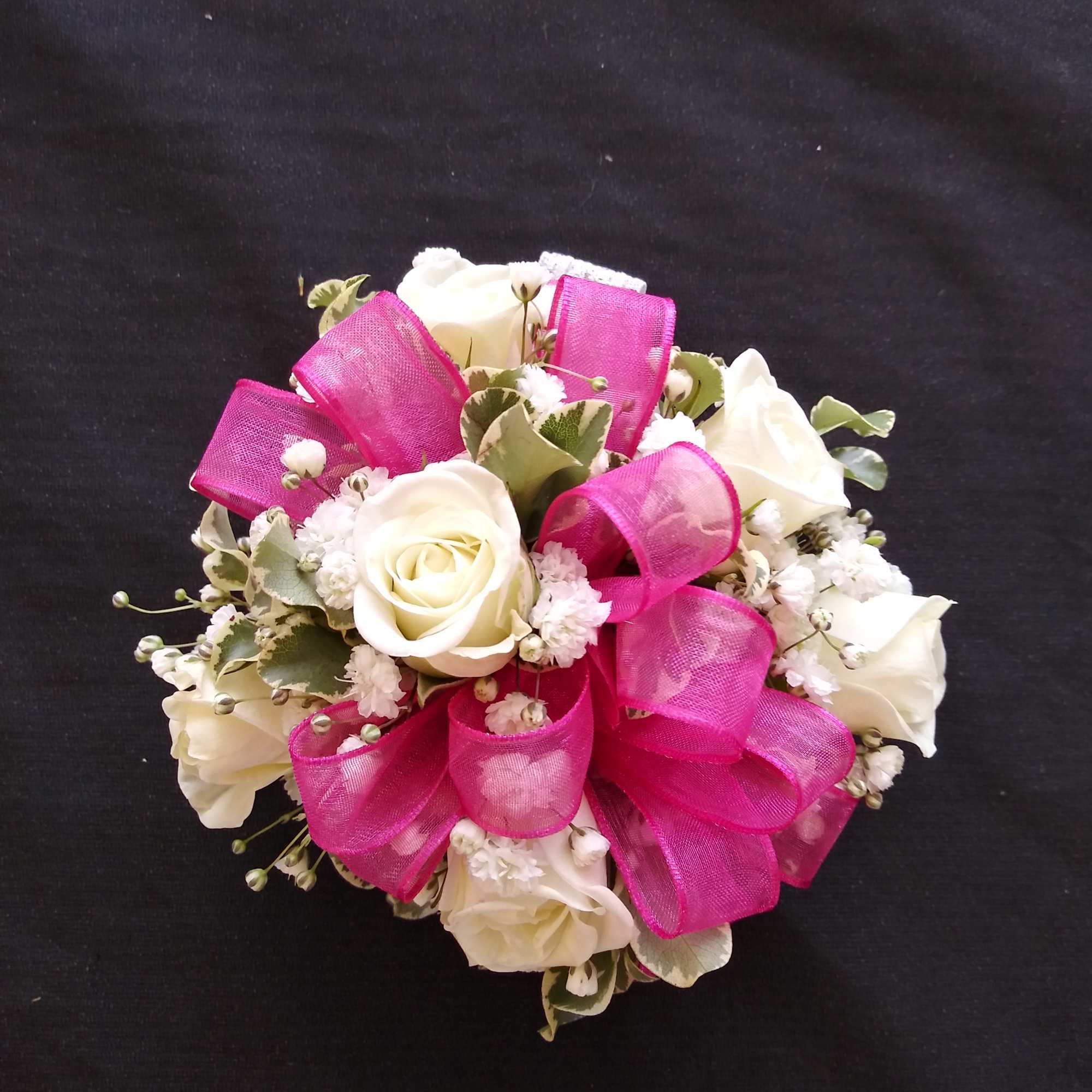 White rose bouquet with bright pink ribbon loops on a black background