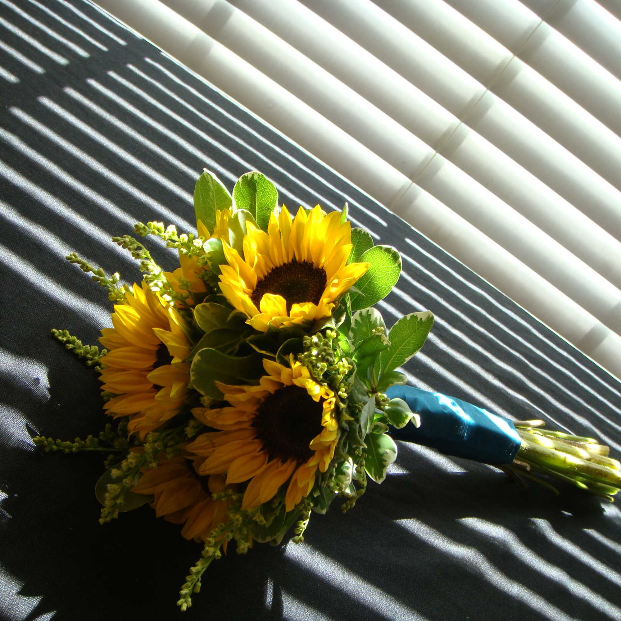 Bouquet of yellow sunflowers with green foliage and a blue ribbon wrap