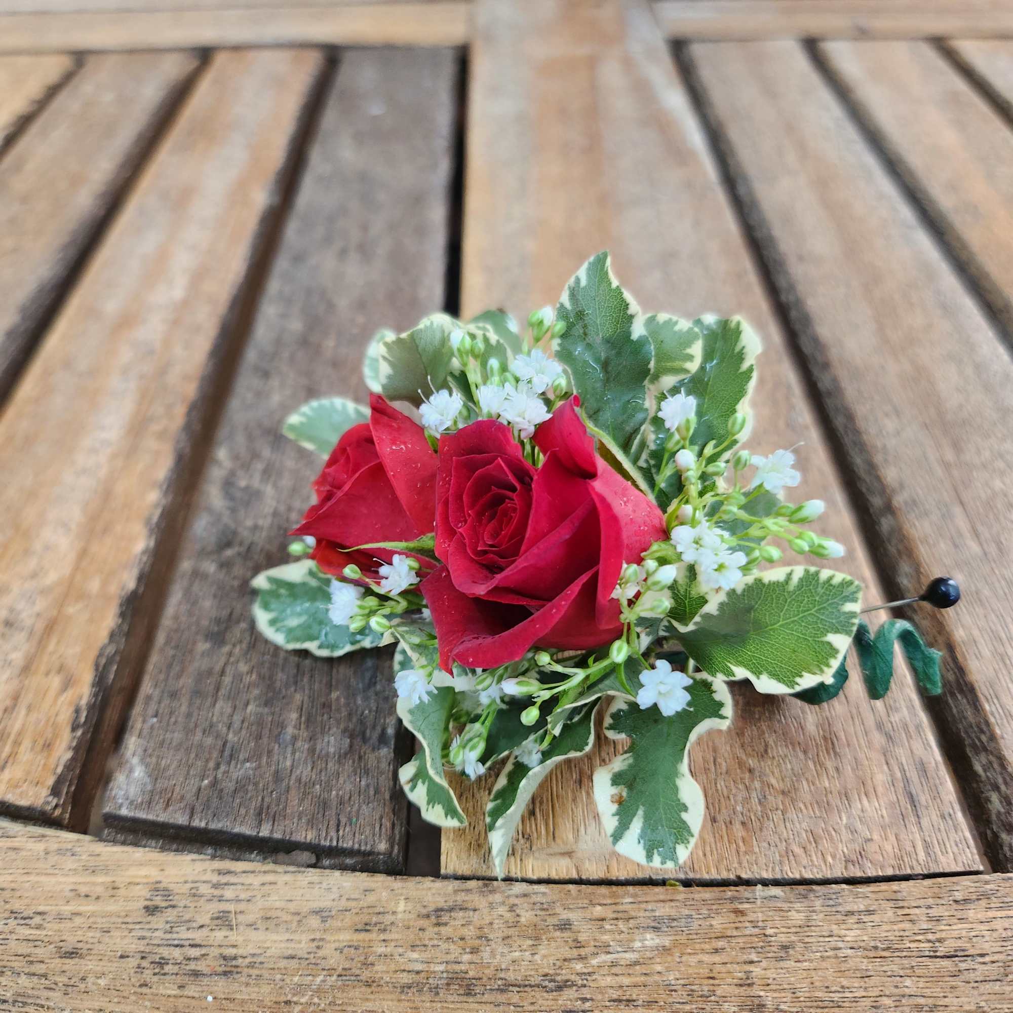 Small red rose boutonniere with white filler flowers and variegated leaves