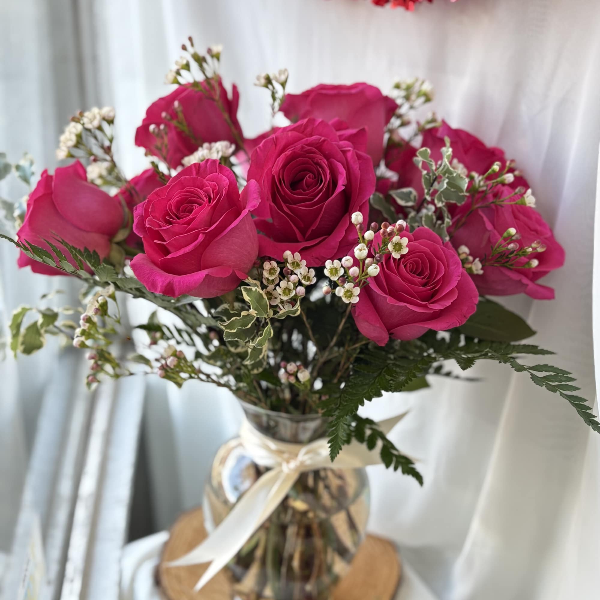 Arrangement of hot pink roses with small white filler flowers in a clear glass vase with a ribbon bow