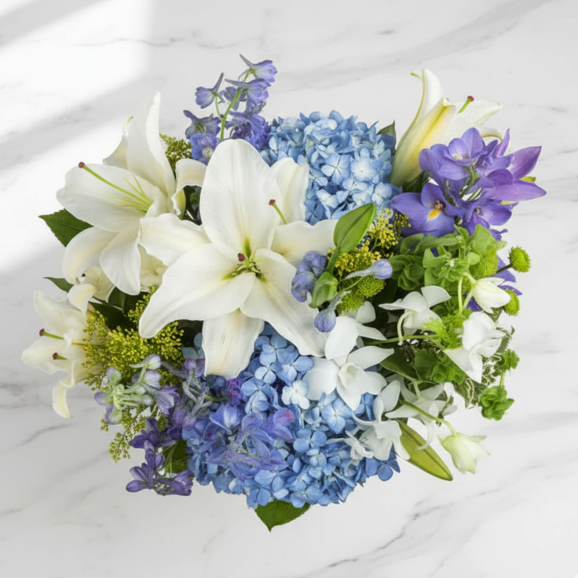 Top view of white lilies, blue hydrangeas, and purple flowers in a compact arrangement.