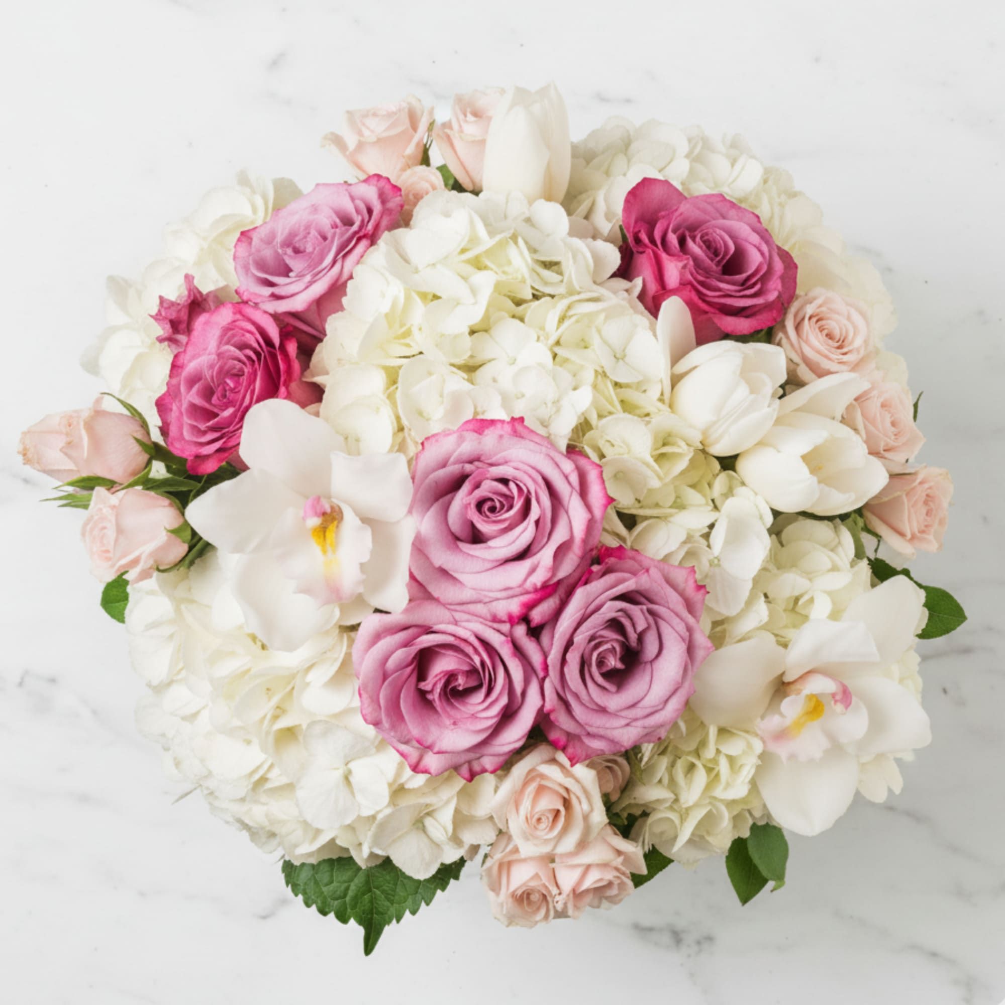 Round arrangement of pink roses, white hydrangeas, tulips, and orchids viewed from above