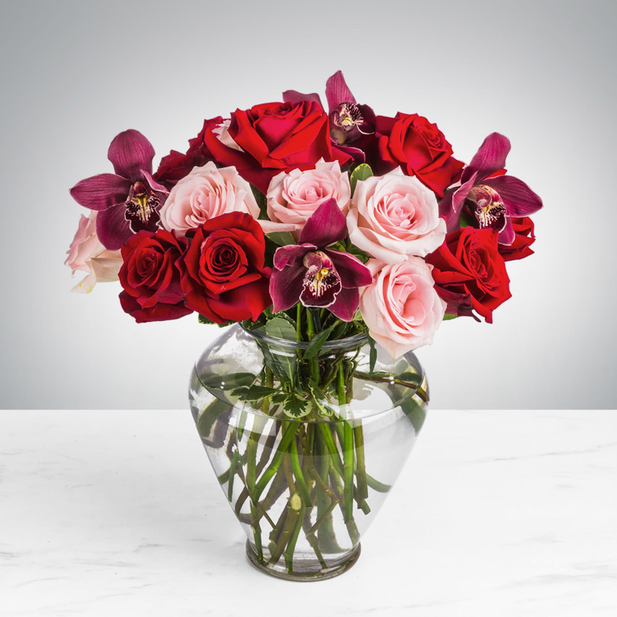 Red roses, pink roses, and purple orchids arranged in a clear glass vase