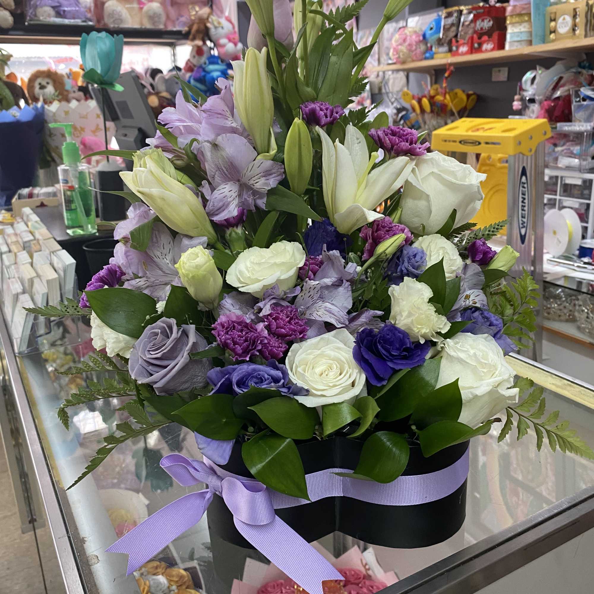 Lavender and white flower arrangement with roses, lilies, and carnations in a black hatbox with purple ribbon