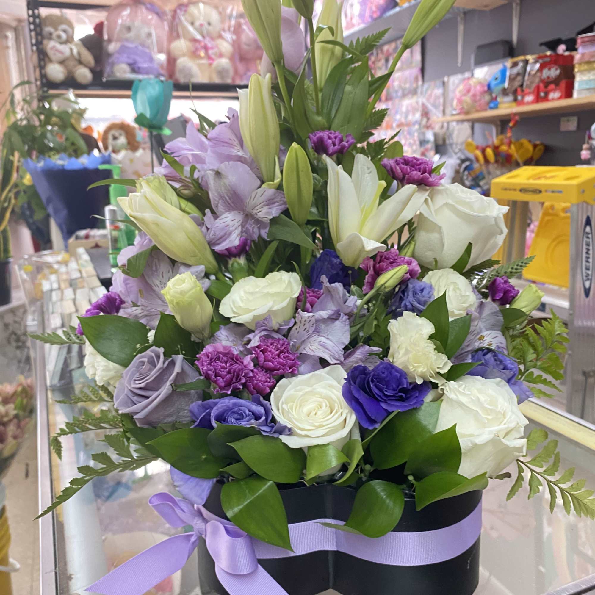 Tall heart-shaped box arrangement of white and purple flowers with a lavender ribbon bow.