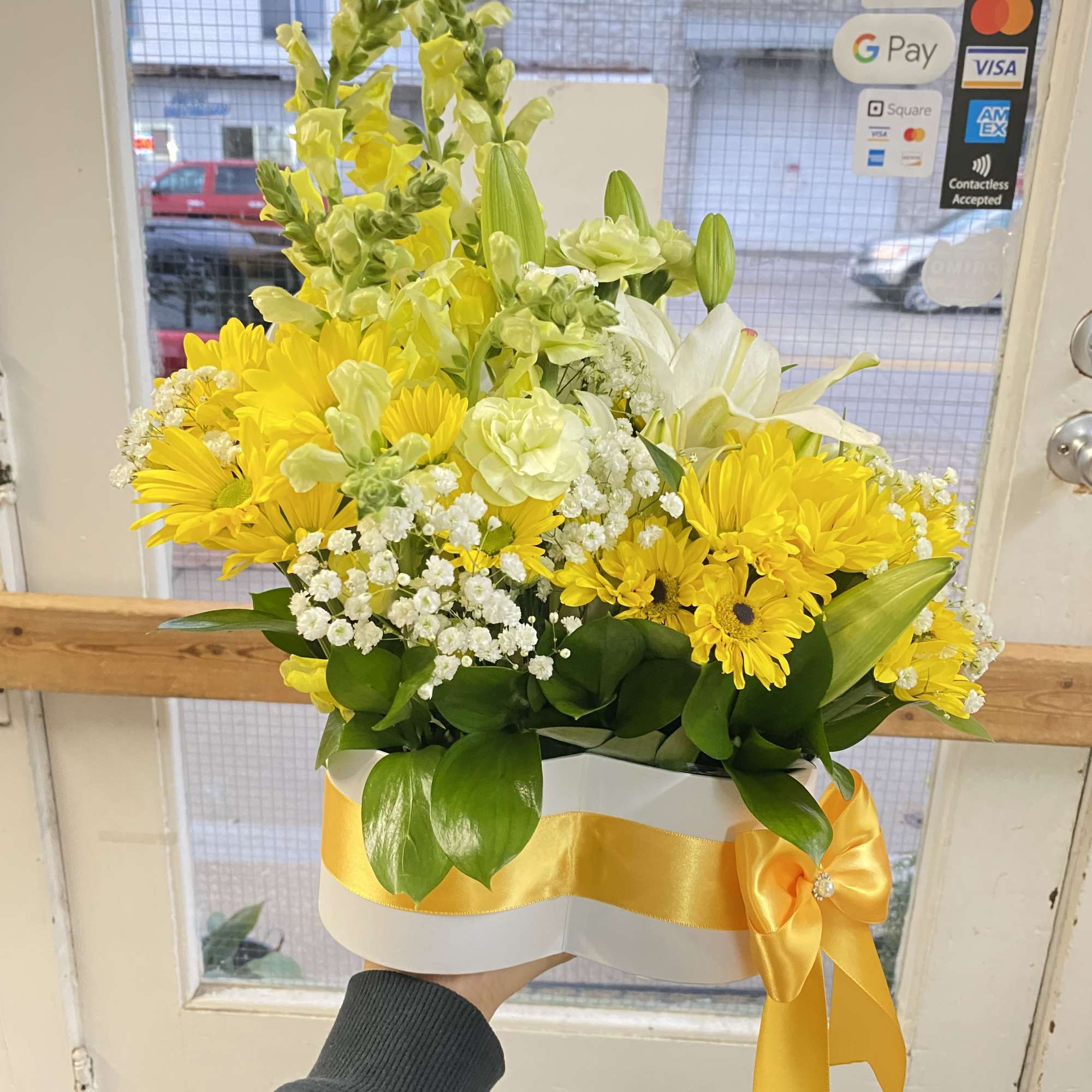 Yellow and white flower arrangement in a white hatbox with a yellow ribbon bow.