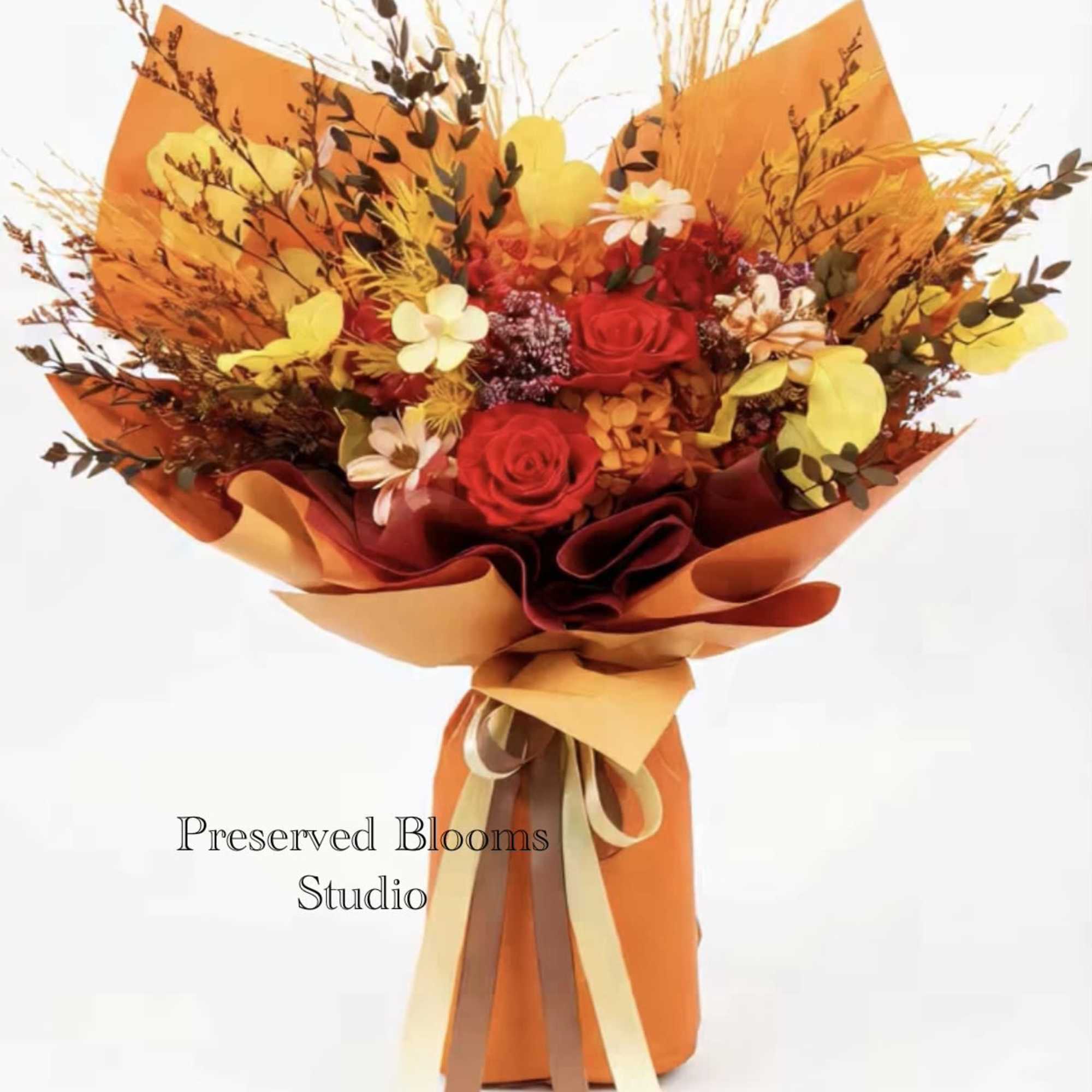 Tall bouquet of red and yellow flowers with dried accents wrapped in bright orange paper with ribbons