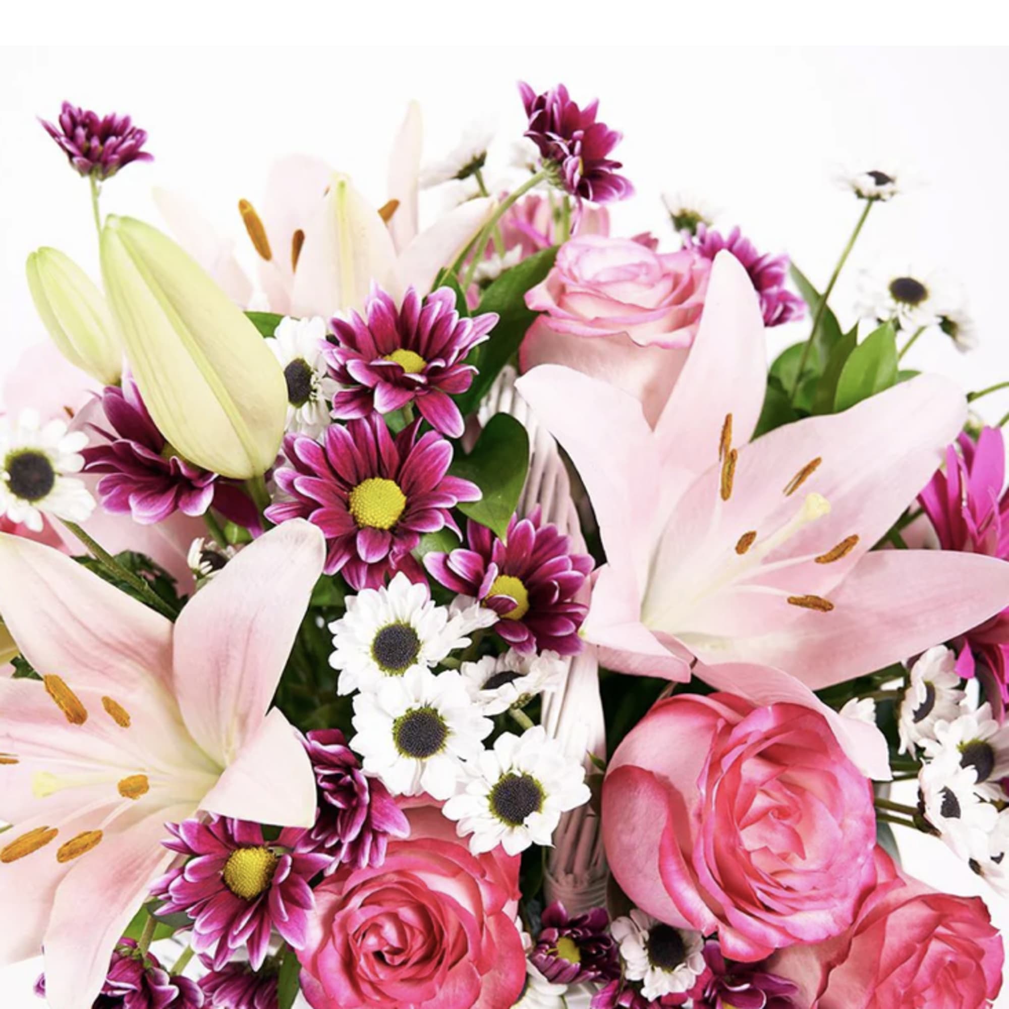 Mixed arrangement of pink lilies, roses, and purple and white daisies in a white basket