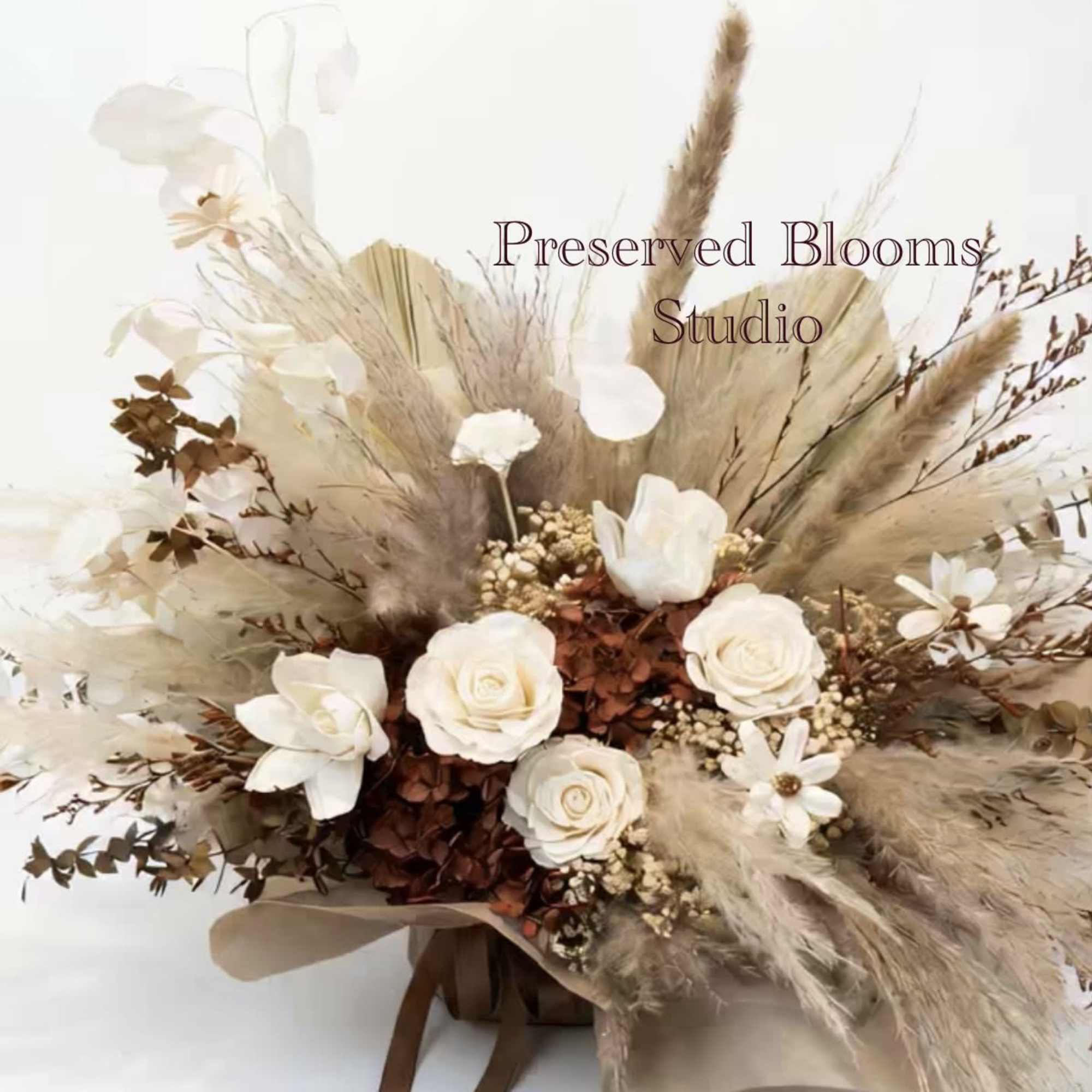 Neutral dried flower arrangement with white roses and beige grasses wrapped in brown paper with ribbons