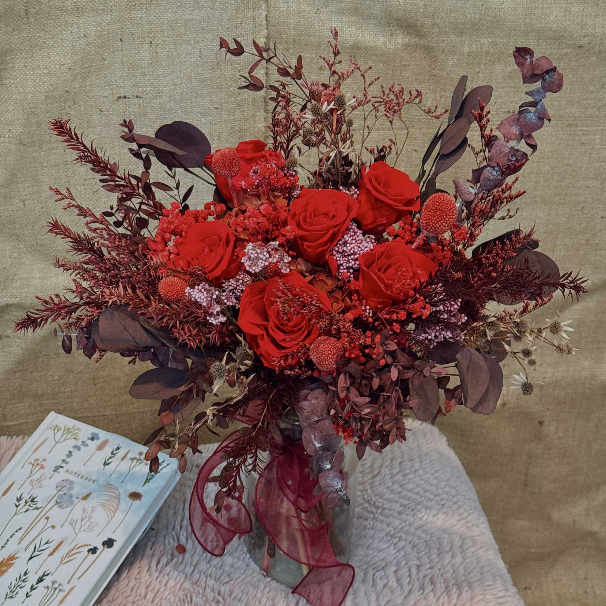 Tall red rose arrangement with burgundy dried accents in a glass vase with ribbon