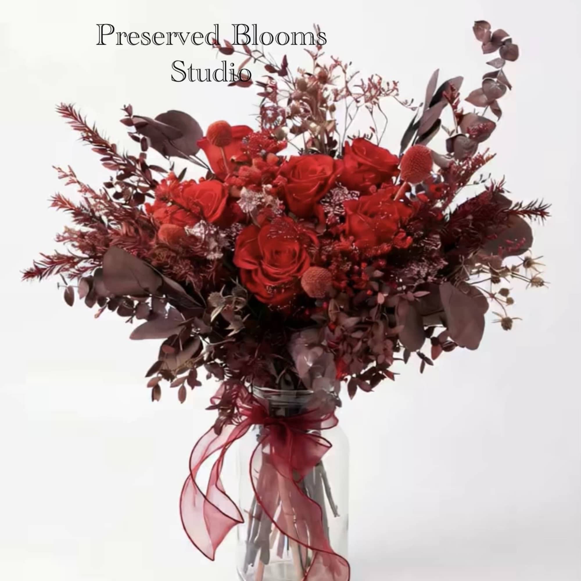Tall bouquet of red roses and burgundy dried elements in a glass jar with red ribbon